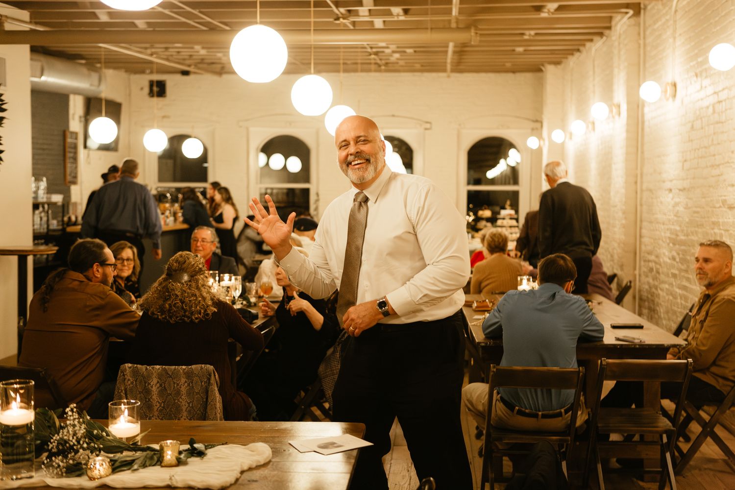 A lively wedding reception scene with hanging globe lights and guests dining at tables.