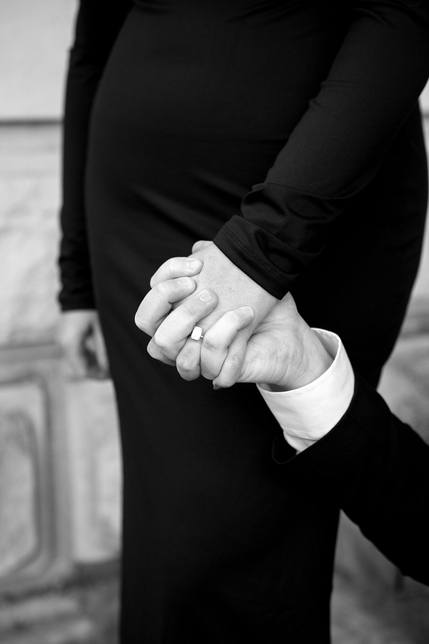 A black and white close-up of clasped hands with an engagement ring.