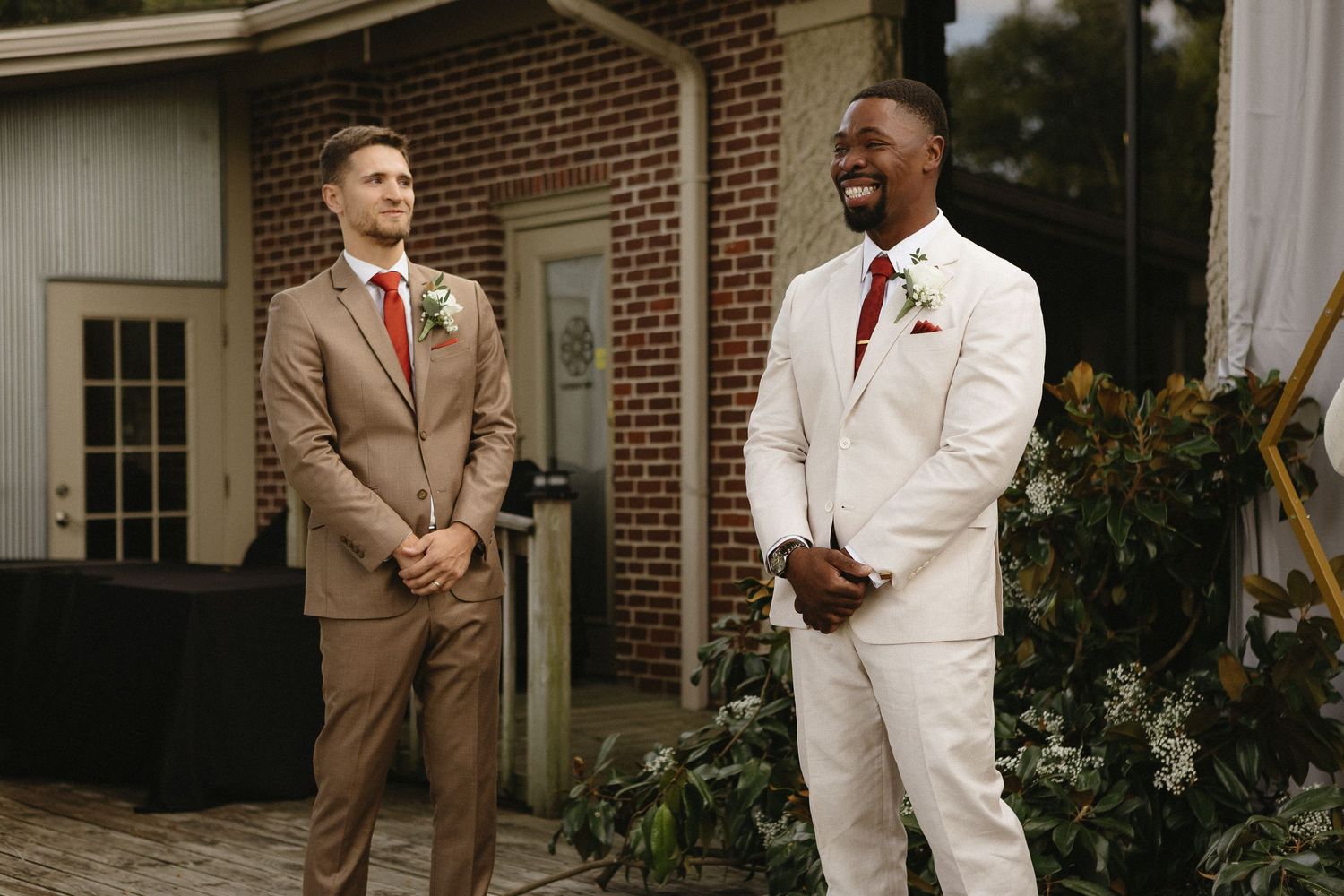 Wedding party members in beige and white suits standing together outdoors.