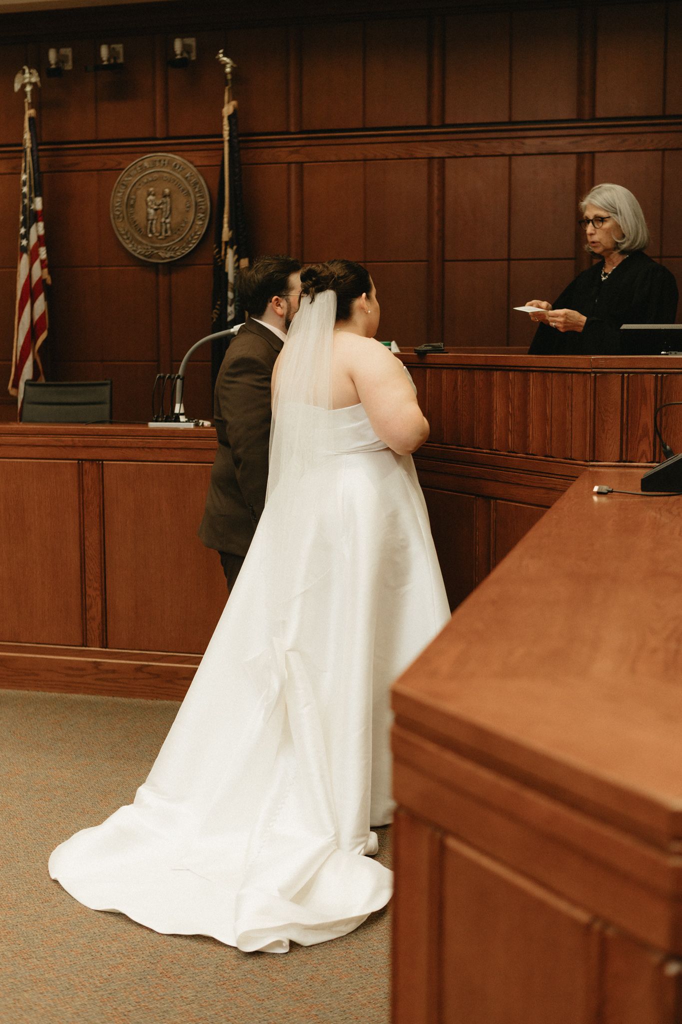 Sequence of a white wedding dress moving through a wood-paneled courtroom.