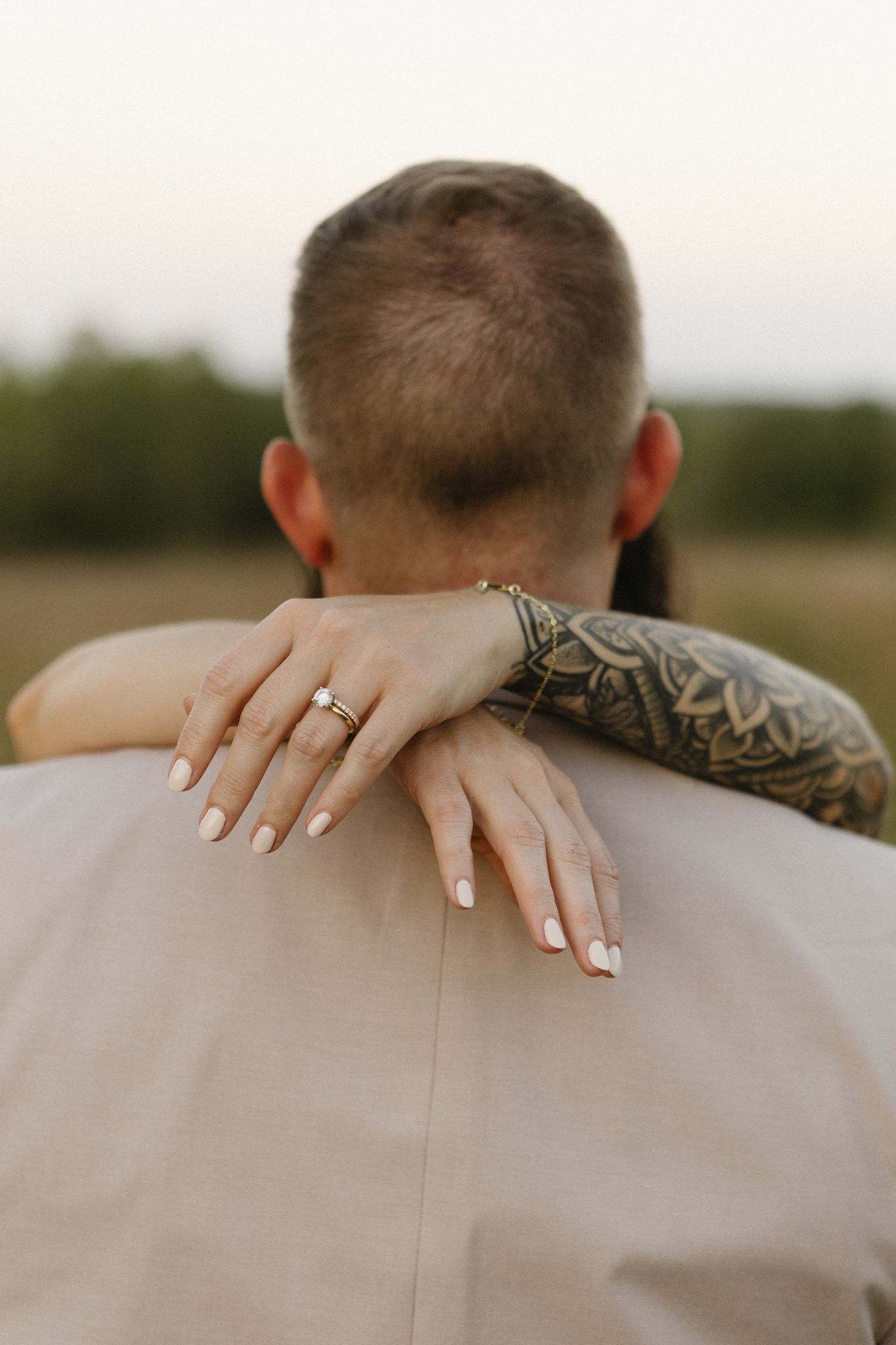 Close-up of hands with wedding ring resting on a beige suit jacket shoulder.