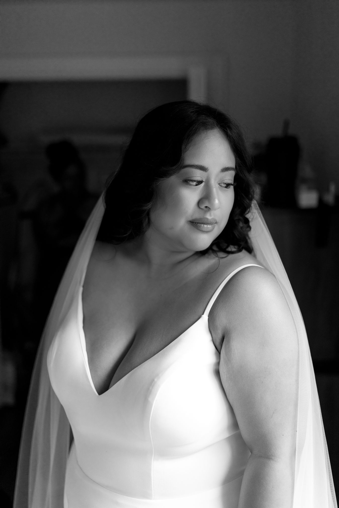 Black and white portrait of a bride in a sleeveless wedding gown with veil looking down pensively.