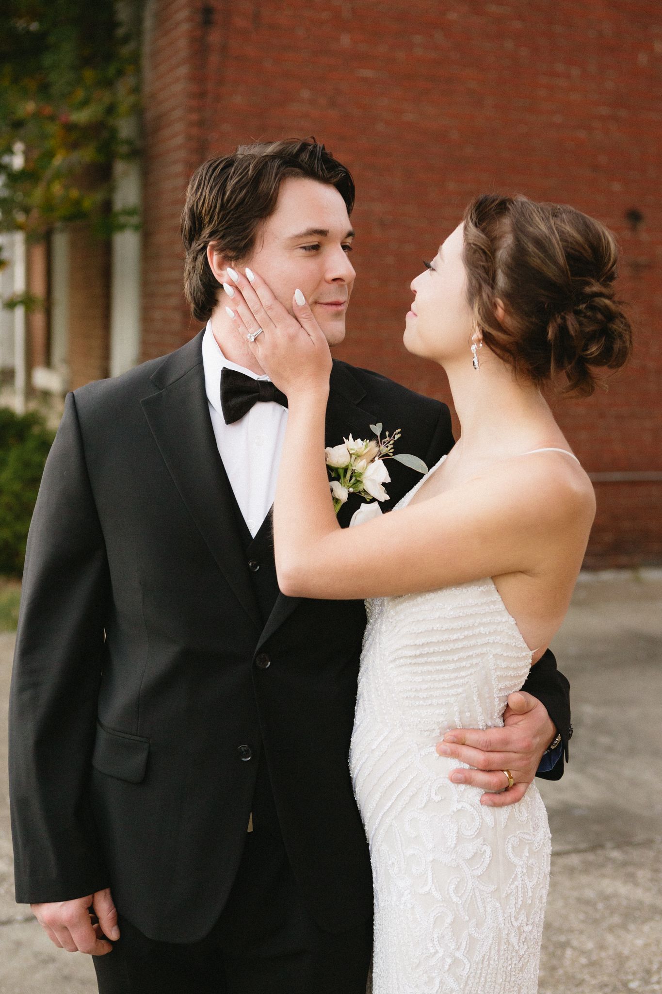 A tender moment between newlyweds as they share an intimate pose in their formal wedding attire against a brick wall.