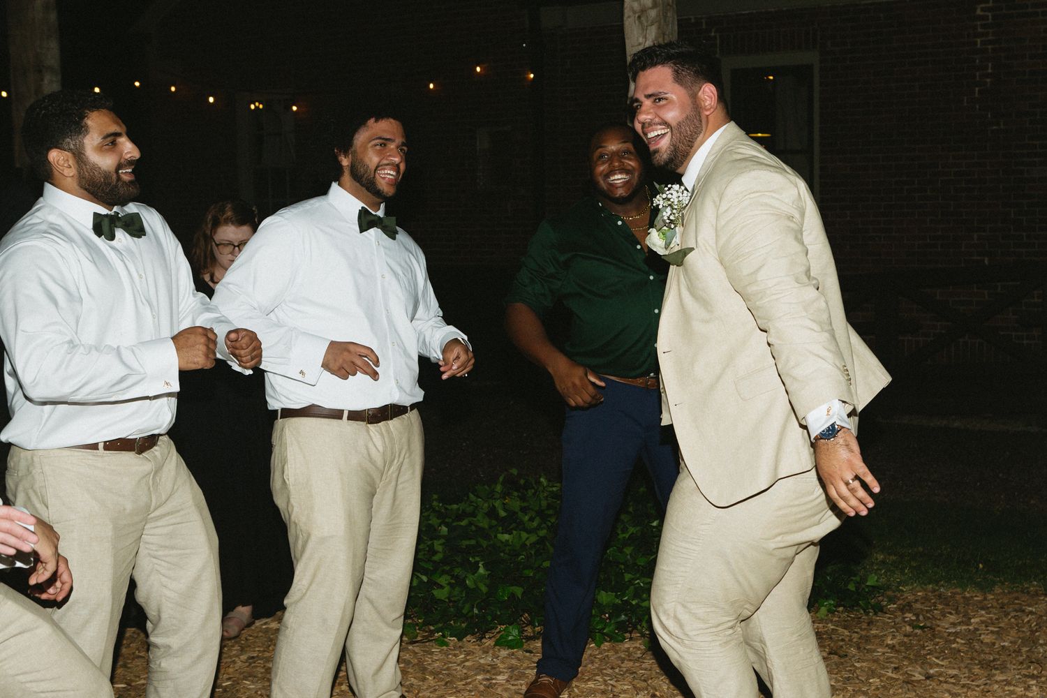A group of people dancing and celebrating at night under string lights at an outdoor party.