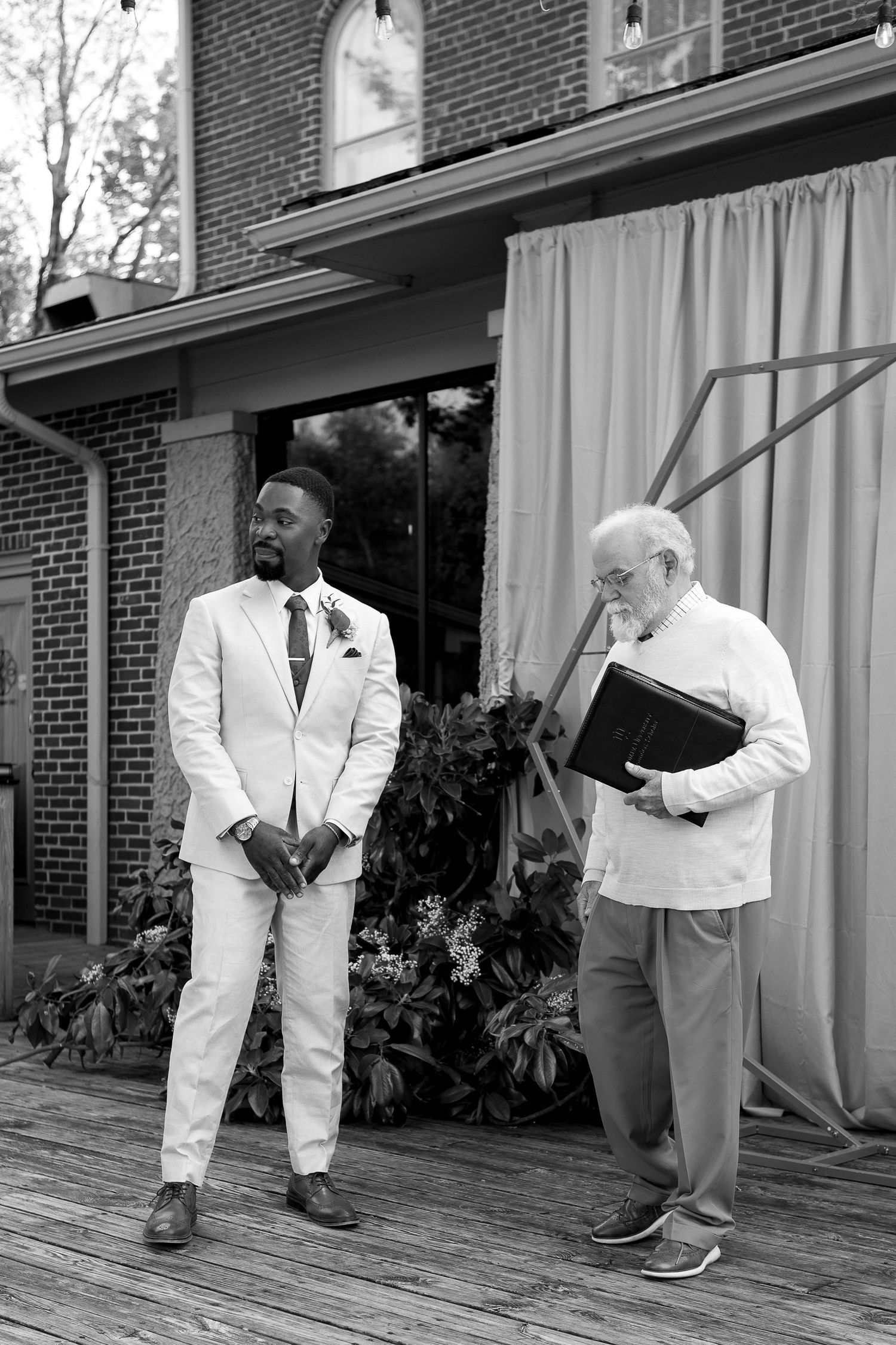 Wedding party members in white suits gather on a brick patio during celebration.