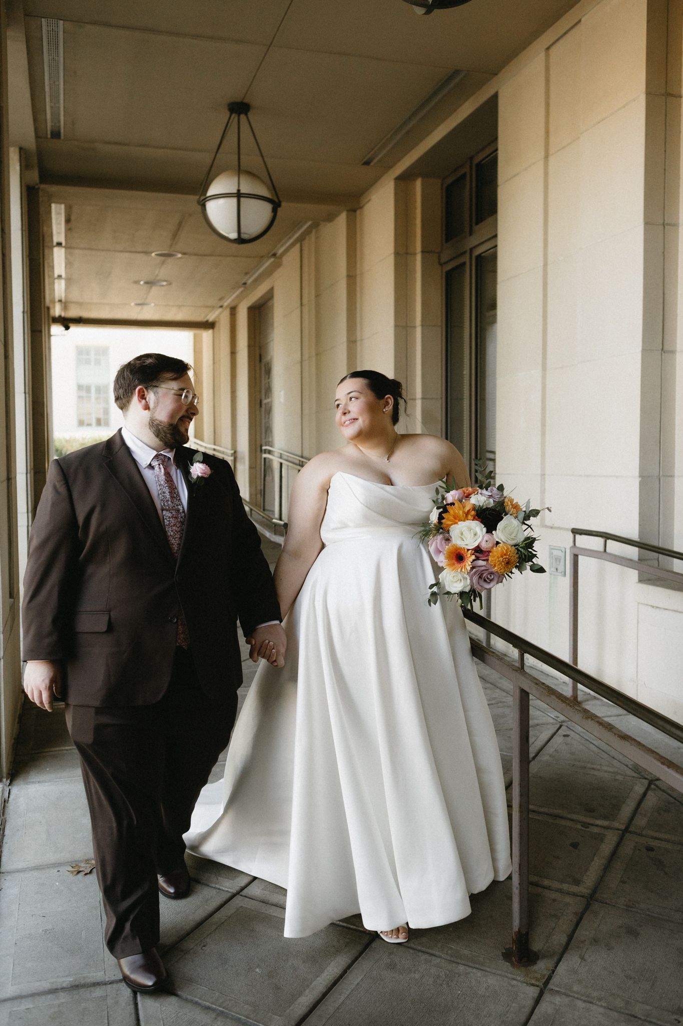 Wedding couple and party members walk through an elegant columned hallway in formal attire.