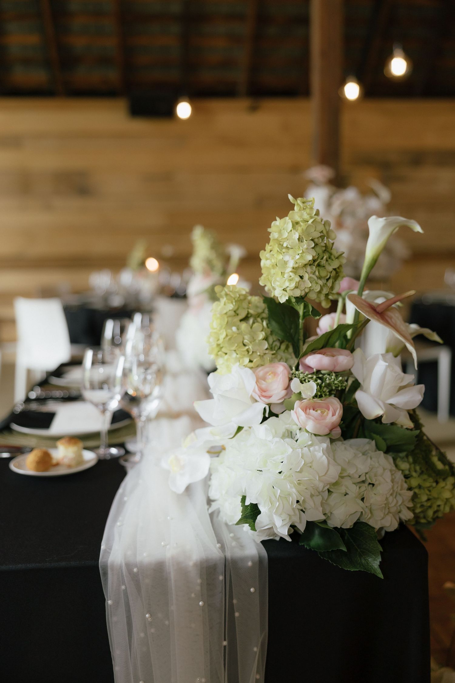 Wedding reception table with black linen, white tulle runner, and lush hydrangea floral centerpiece.