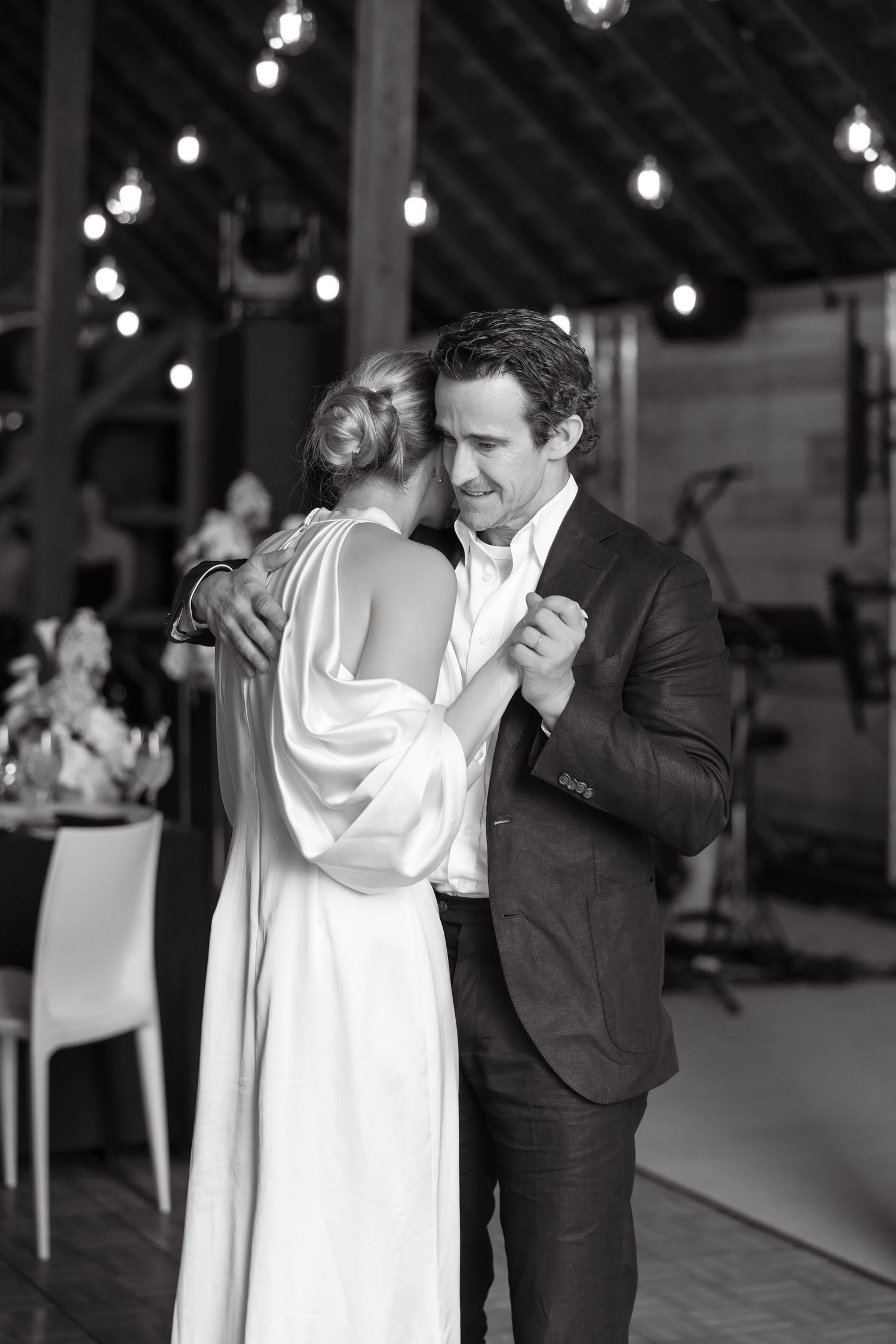 Black and white romantic first dance photo of bride and groom in rustic barn wedding venue.