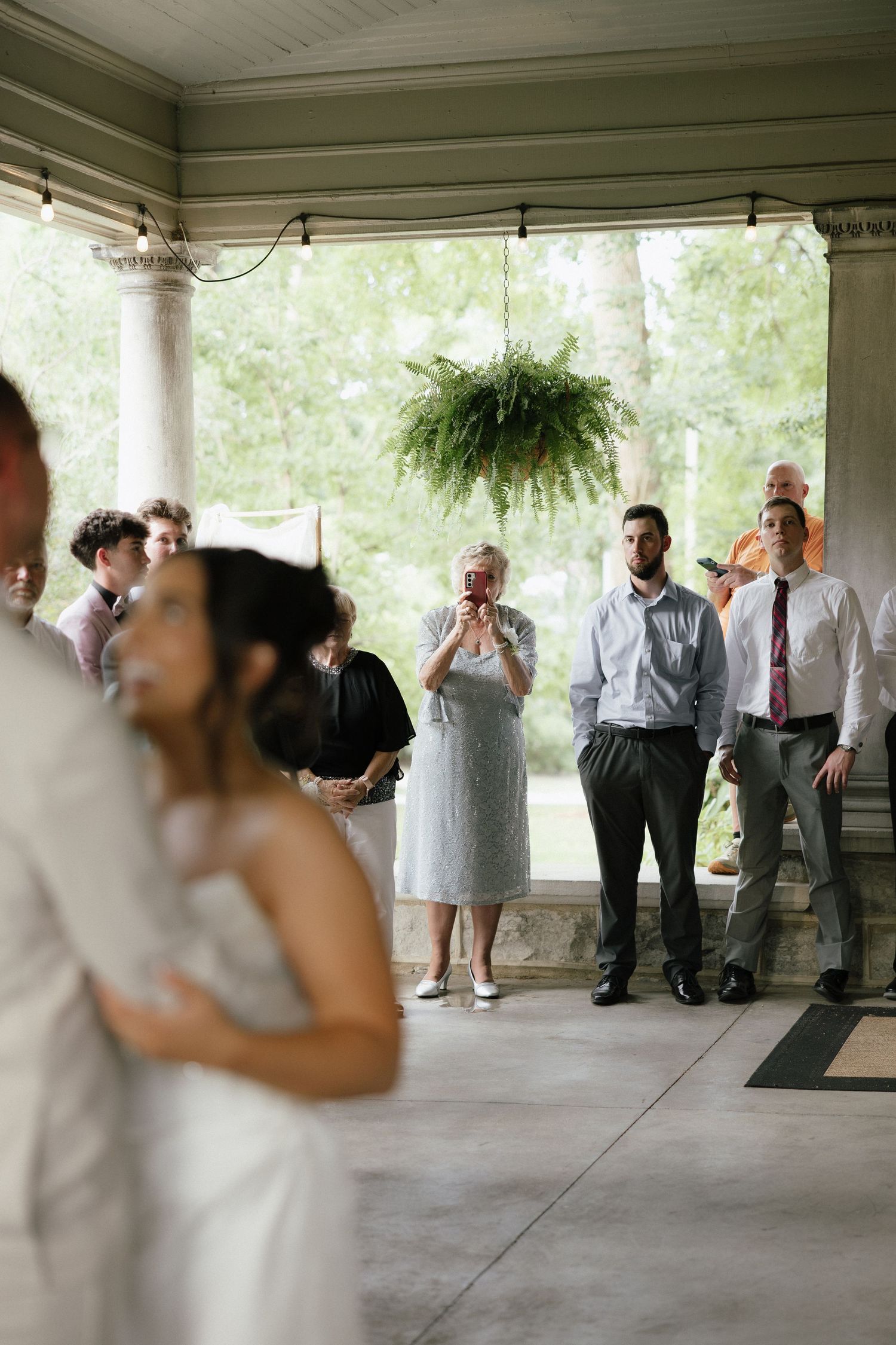 Wedding guests watch bride and groom share first dance on elegant covered porch venue.
