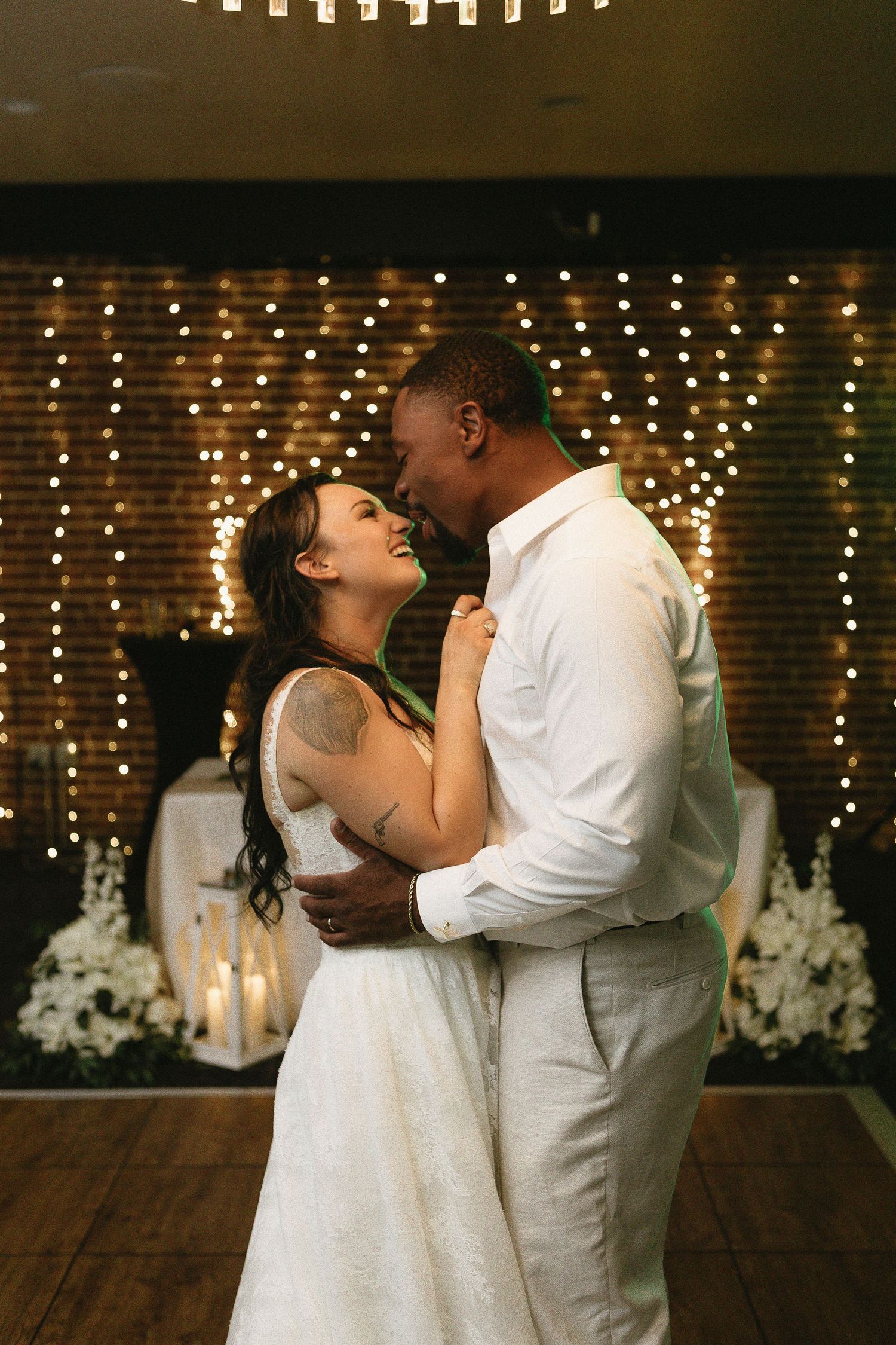Romantic dance moment under twinkling lights and brick wall backdrop.