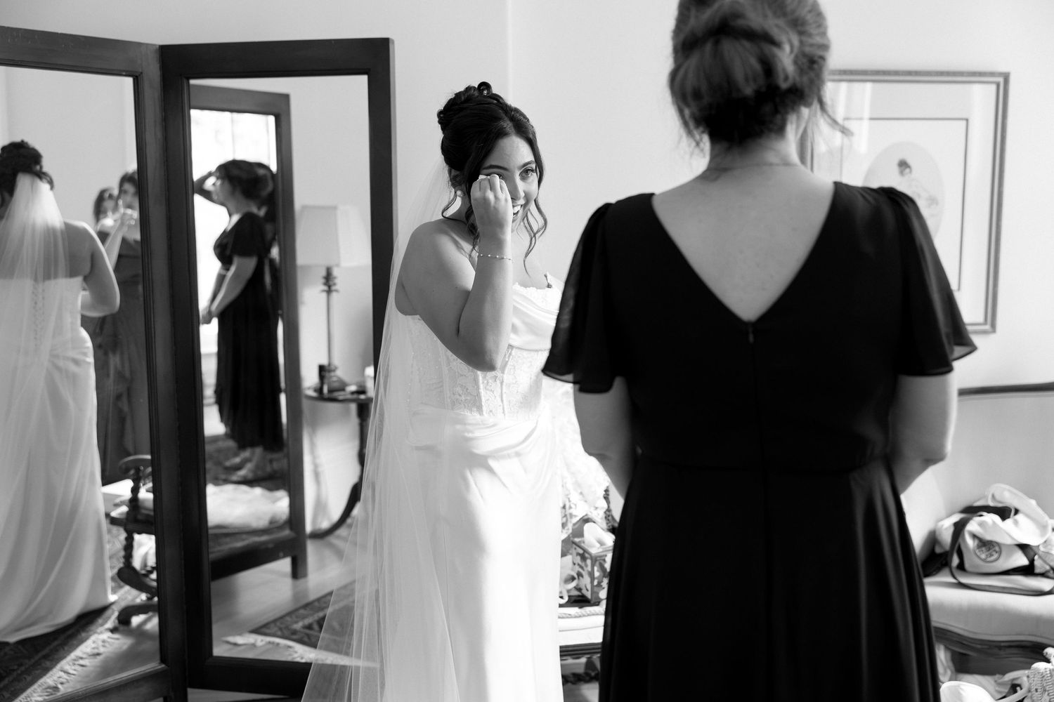 Black and white photo of an emotional bride wiping tears while a bridesmaid in black dress watches during wedding preparations.