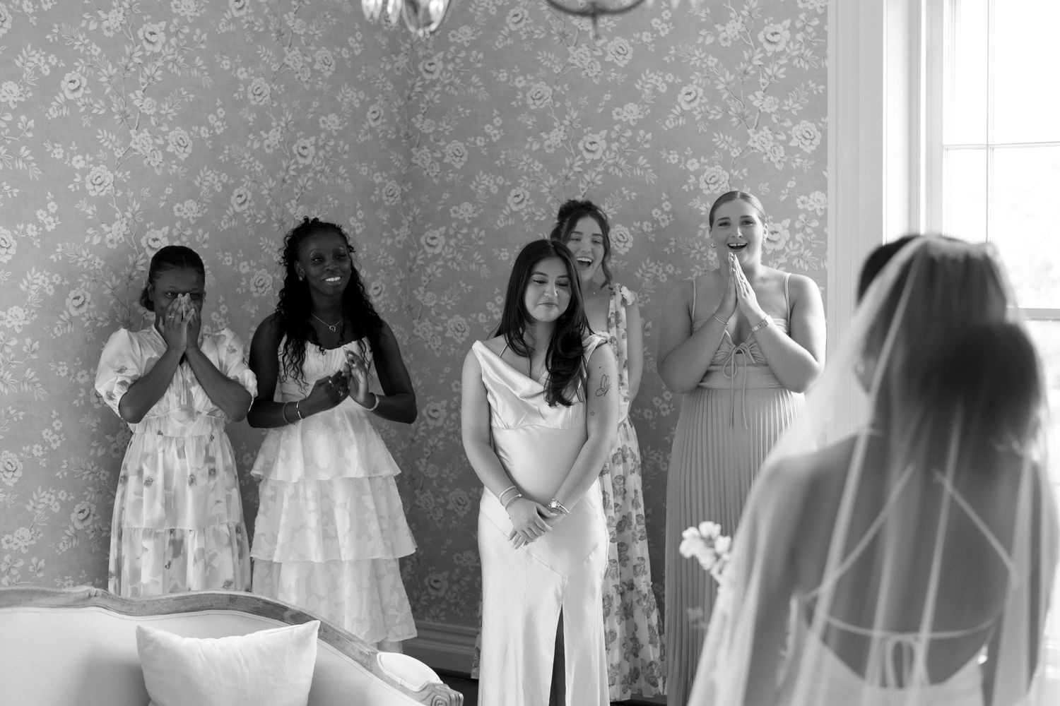 Group in formal attire gathered in an elegant room with decorative wallpaper.