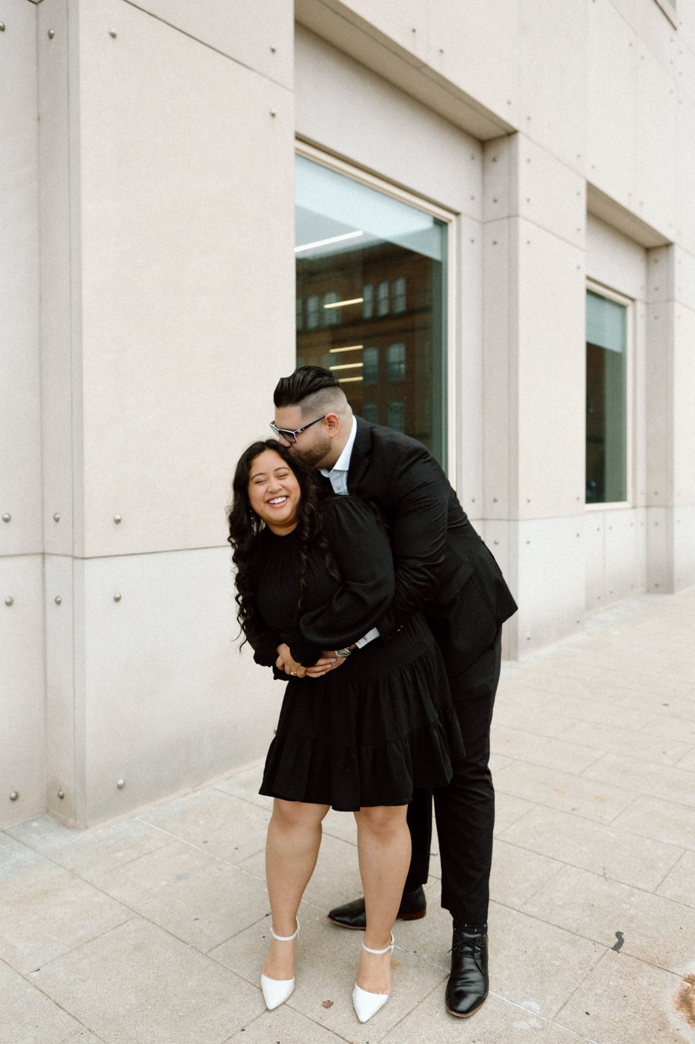 Engaged couple in downtown Louisville, with the woman smiling and showing her engagement ring while embracing her fiancé