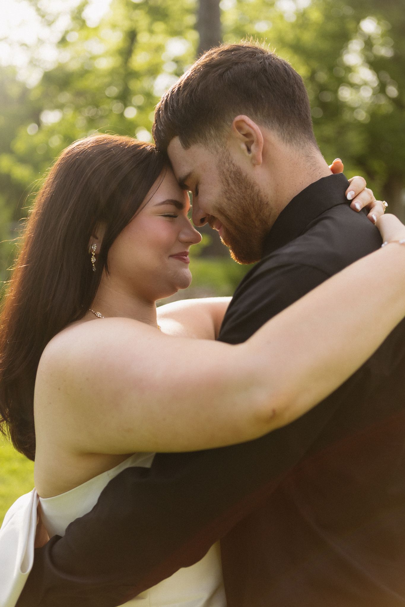 A couple sharing an intimate romantic moment outdoors with sunlit trees in the background.