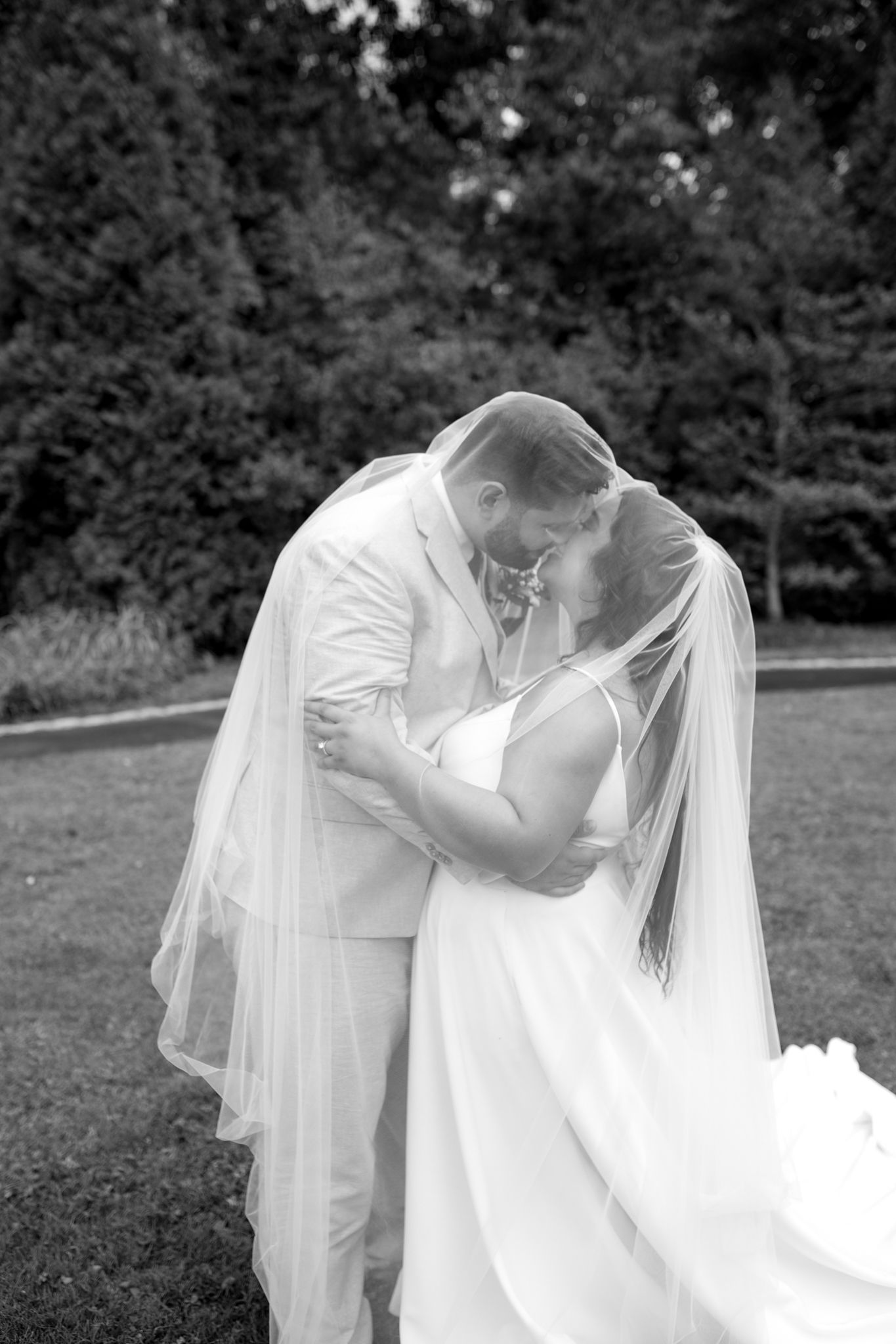 A tender romantic moment between a bride and groom sharing a kiss outdoors in black and white photography.