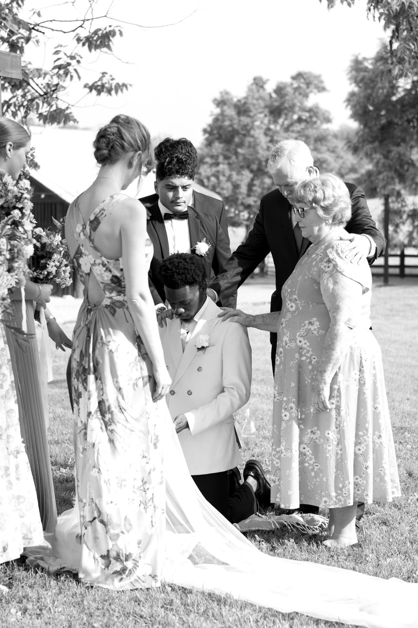 Black and white photo showing wedding party lineup with elegant bridal veils on grassy field.