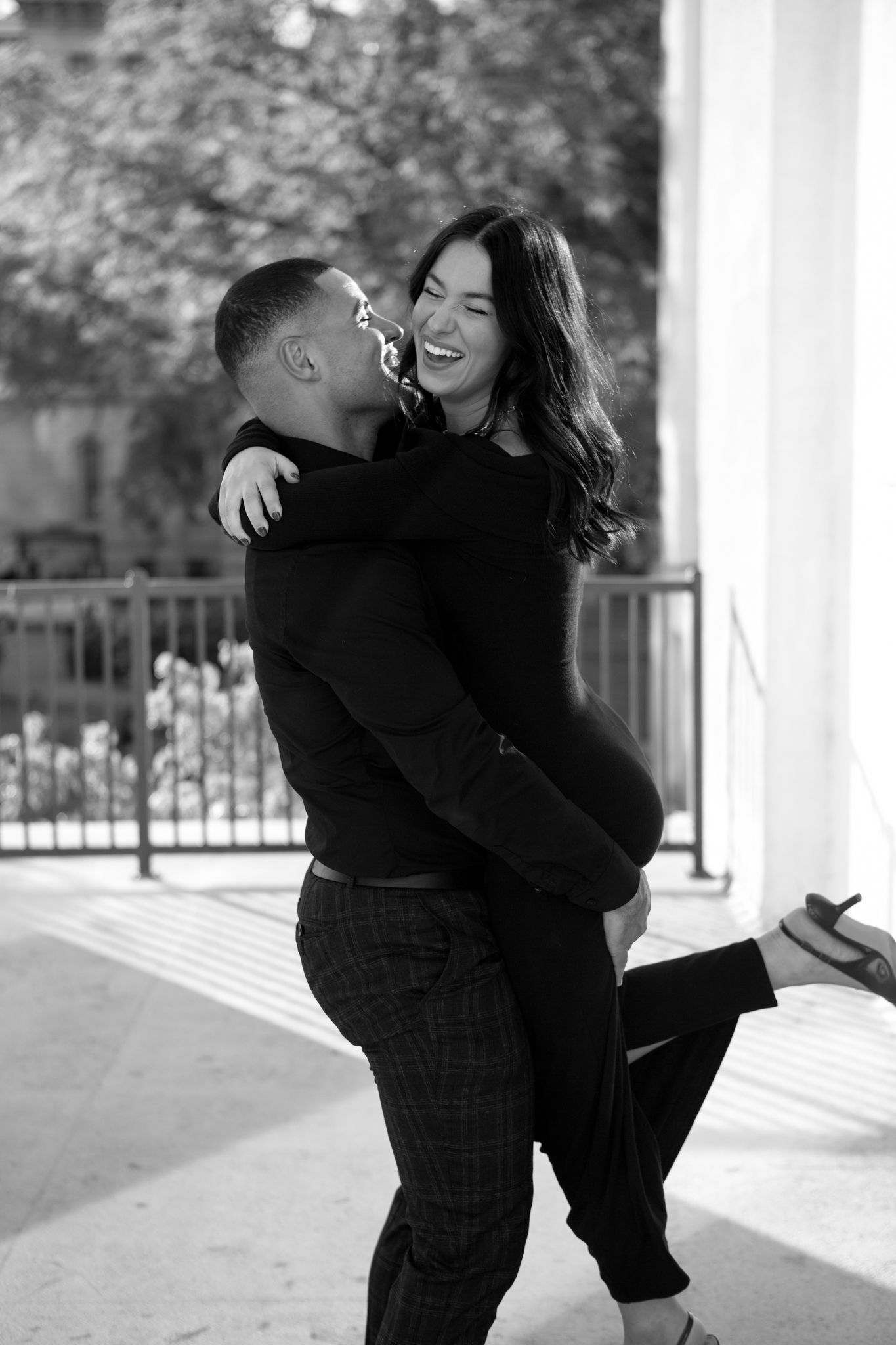 A joyful black and white photo of a couple laughing and embracing on a porch.