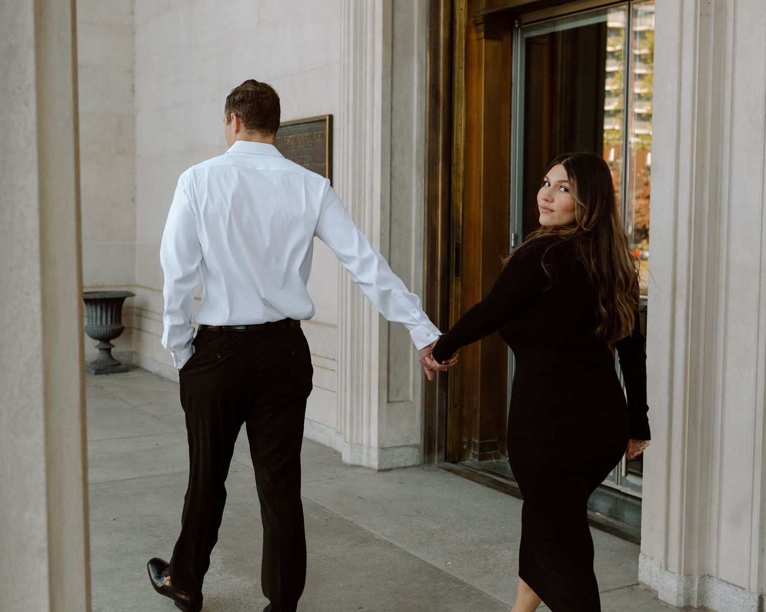 Engaged couple in downtown Louisville, with the woman smiling and showing her engagement ring while embracing her fiancé