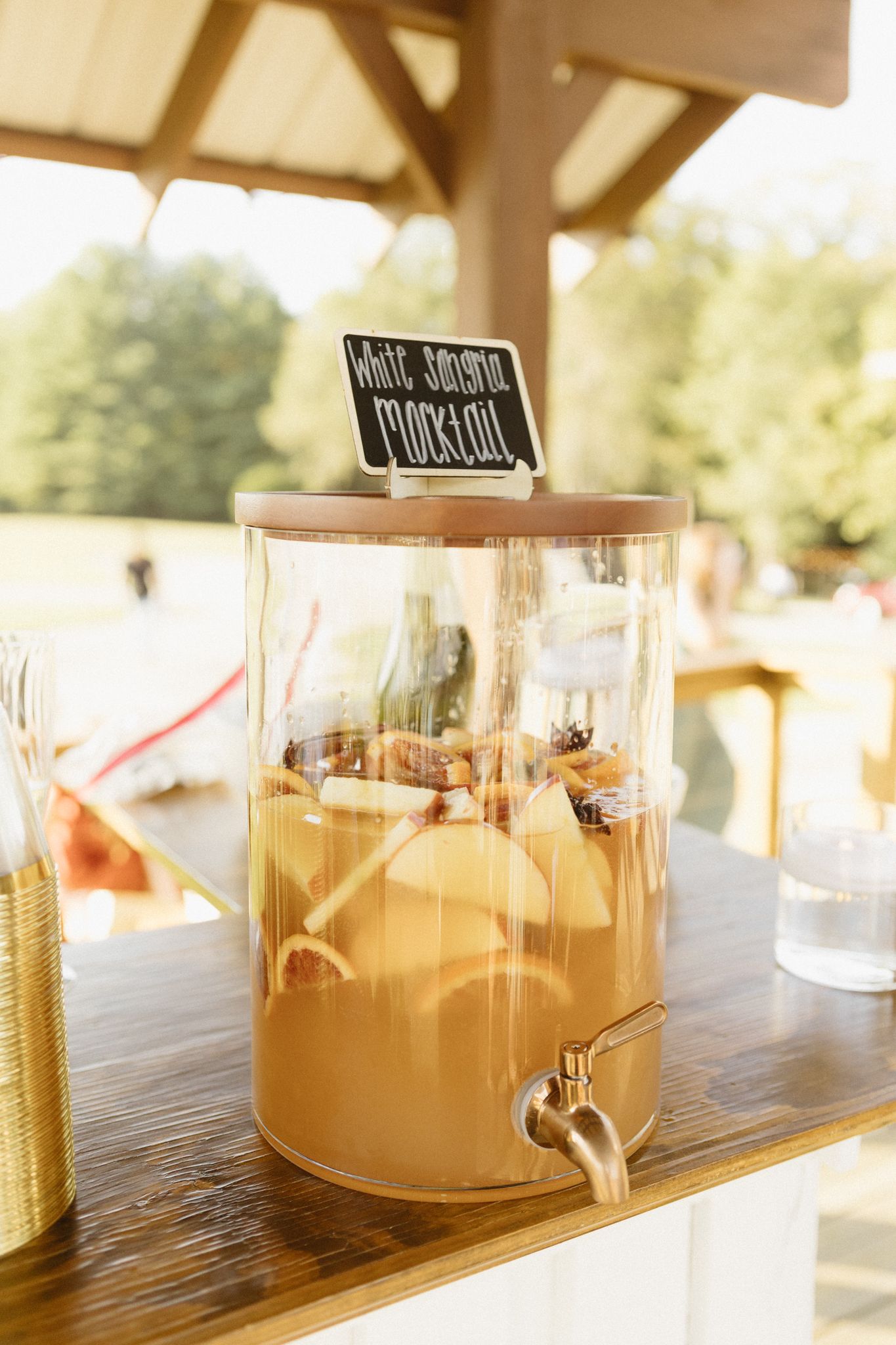 Glass drink dispensers filled with lemonade or juice lined up on a wooden surface in sunlit outdoor setting.