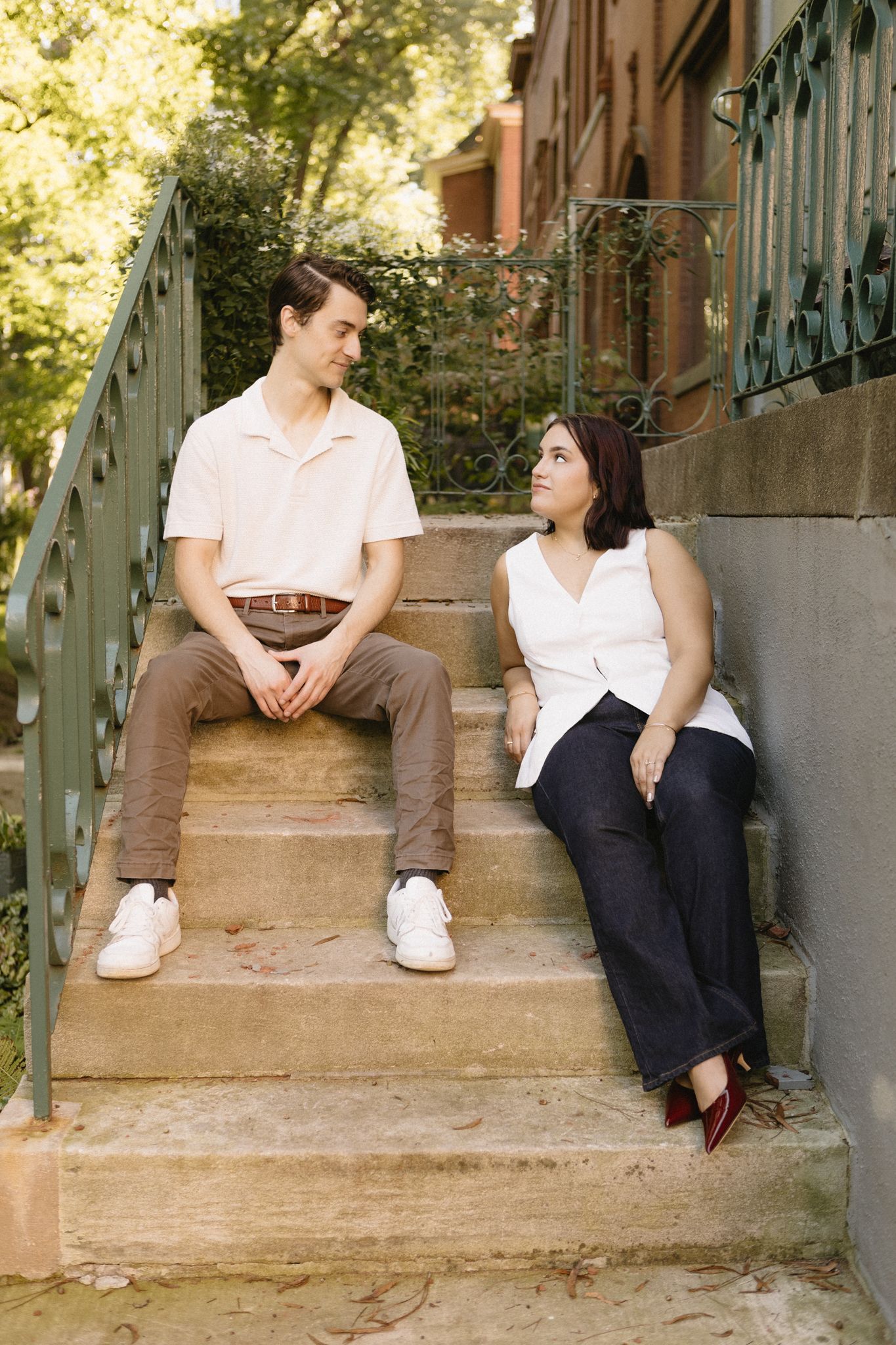 A couple sits and chats on concrete steps outdoors in a casual setting with natural lighting.