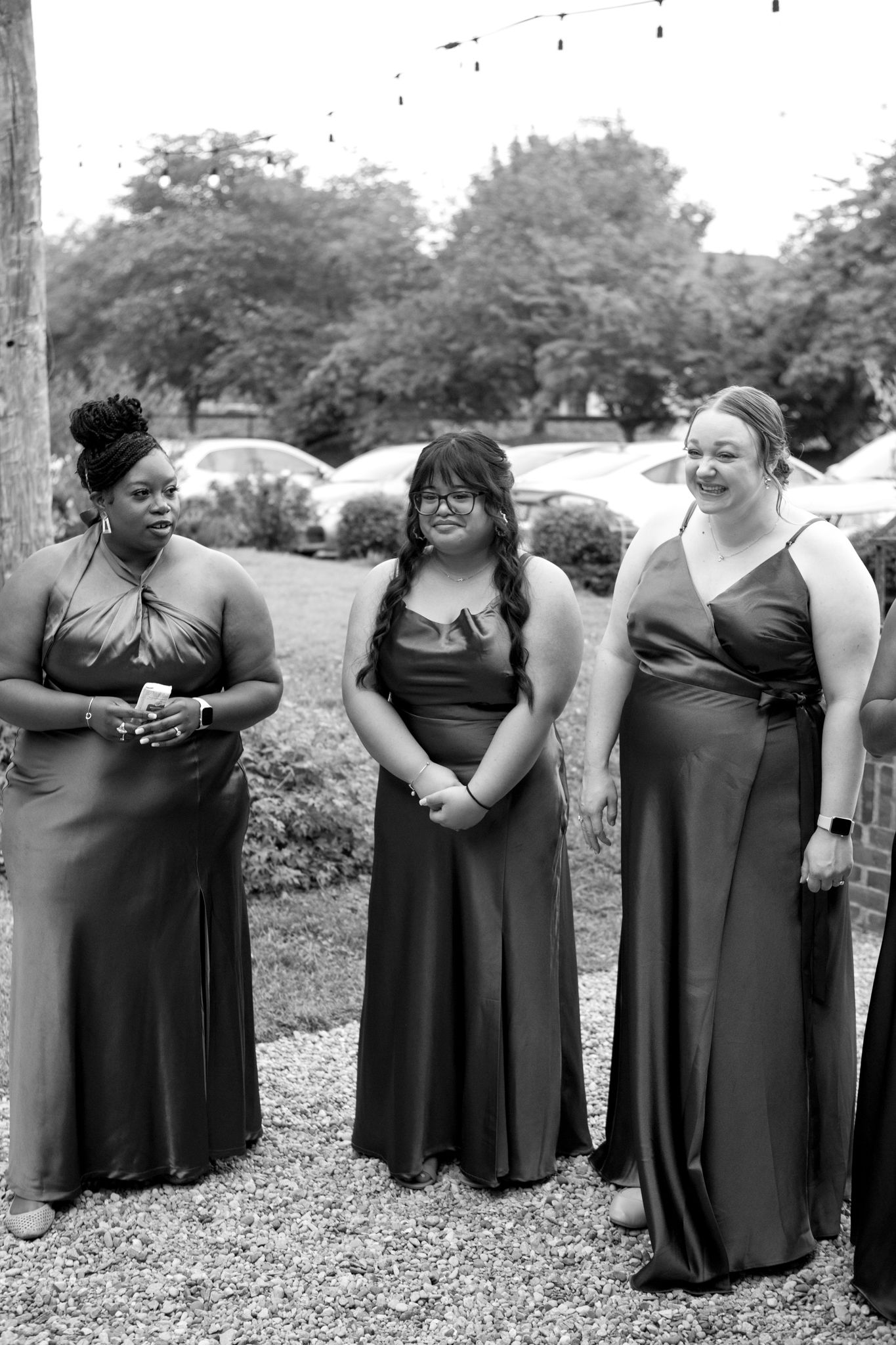 Three women wearing elegant full-length black dresses stand together at an outdoor event.