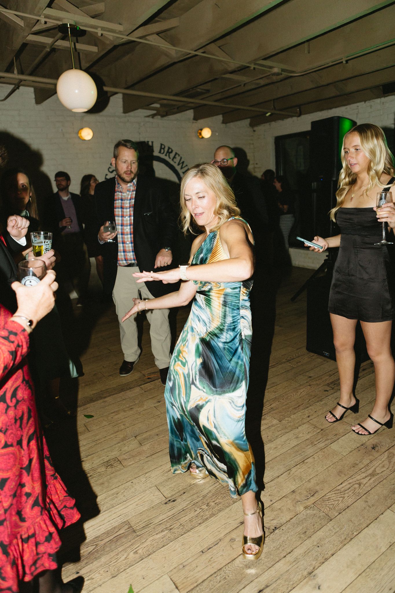 Party guests dancing in a rustic venue with exposed beams and wooden floors.