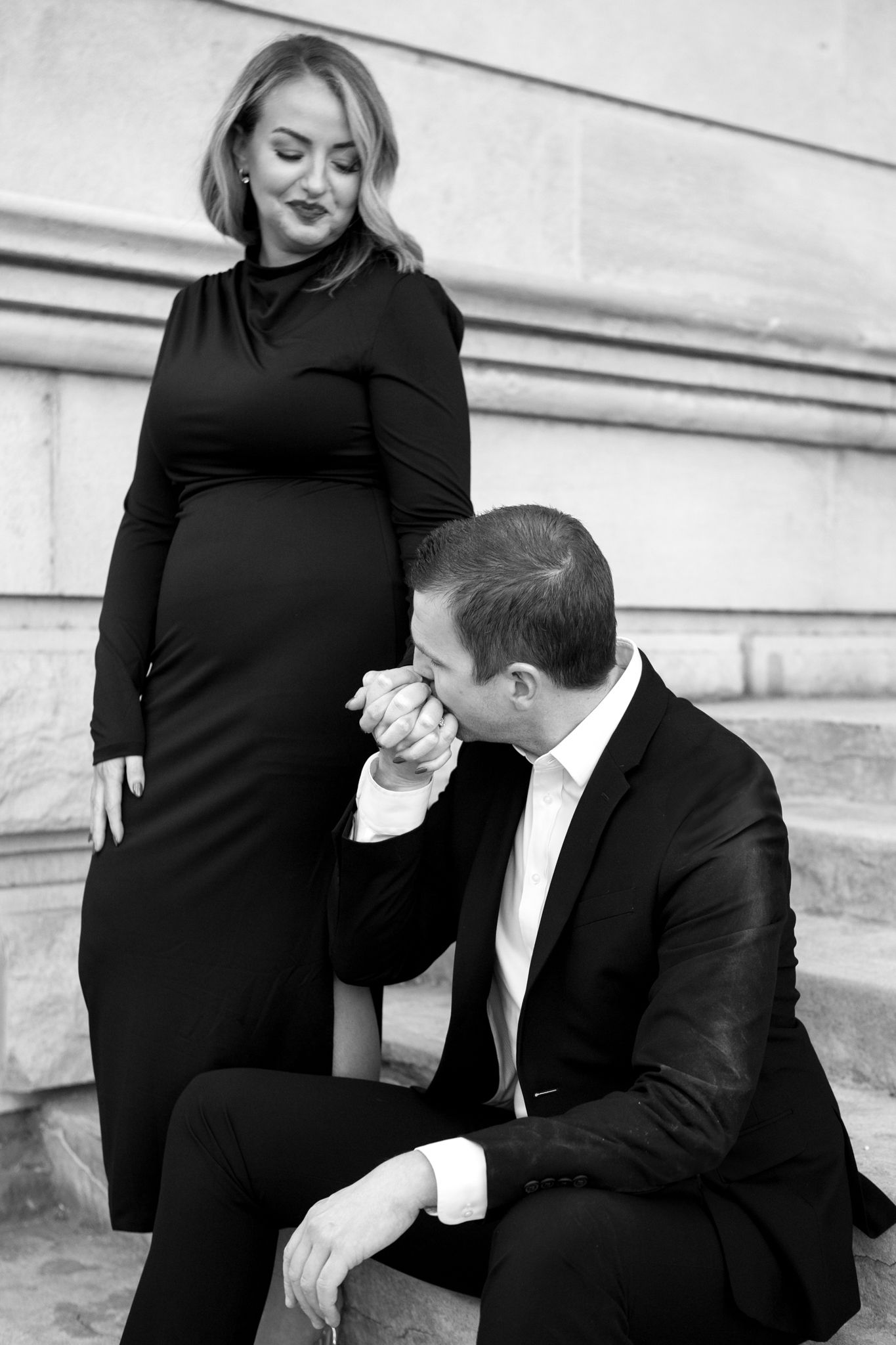 A romantic black and white photo of a couple in formal attire on stone steps, with a tender moment captured.