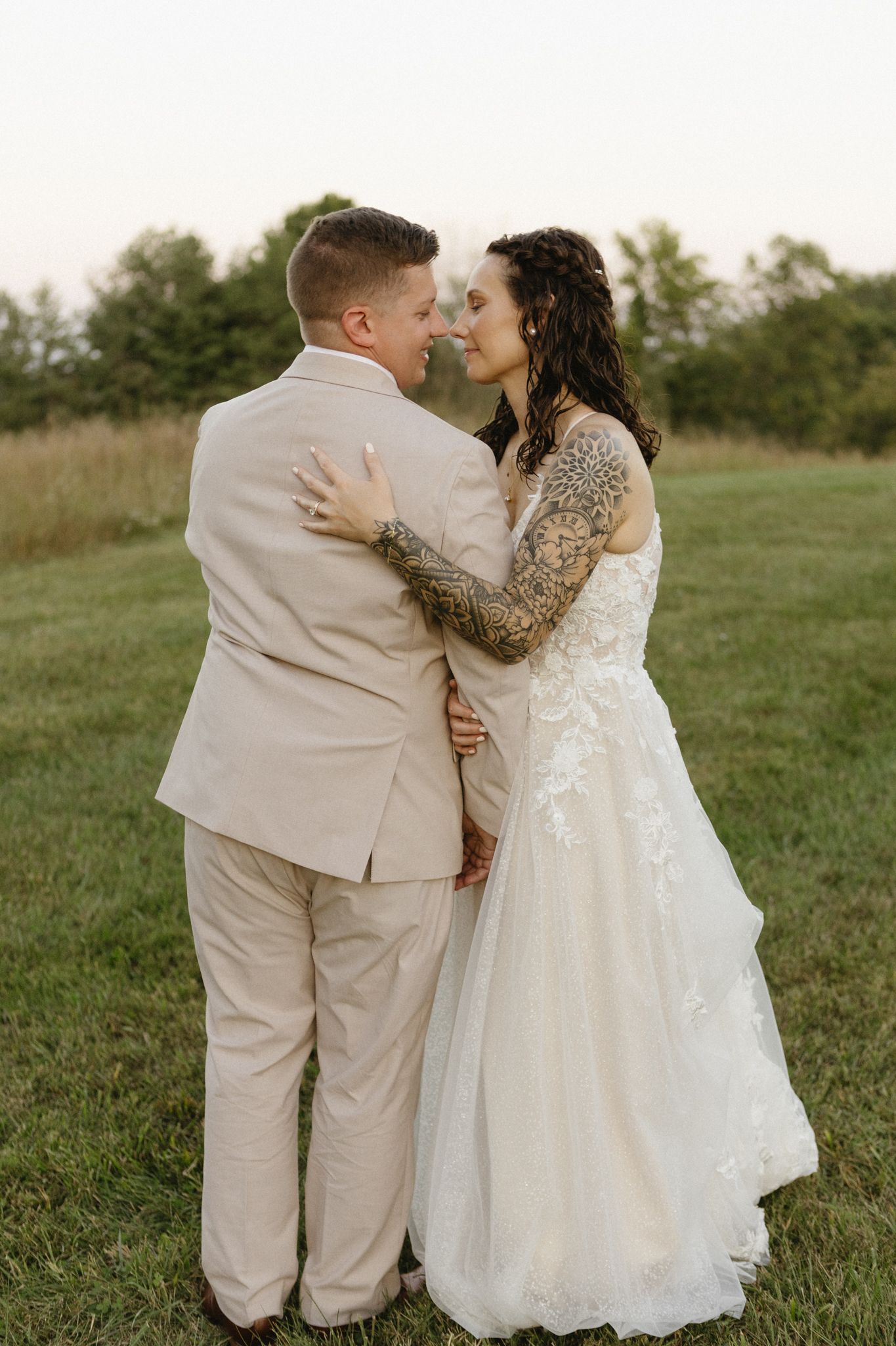 Intimate wedding couple moment captured in golden hour light on grassy field.