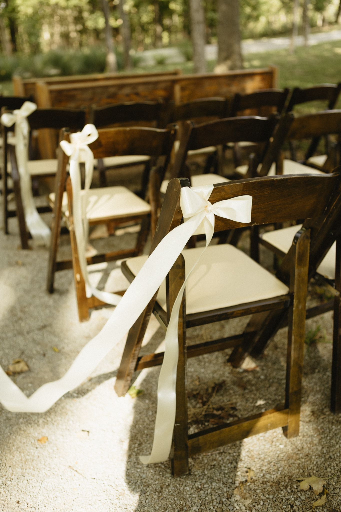 White wooden folding chairs arranged in rows for an outdoor ceremony with decorative ribbons.