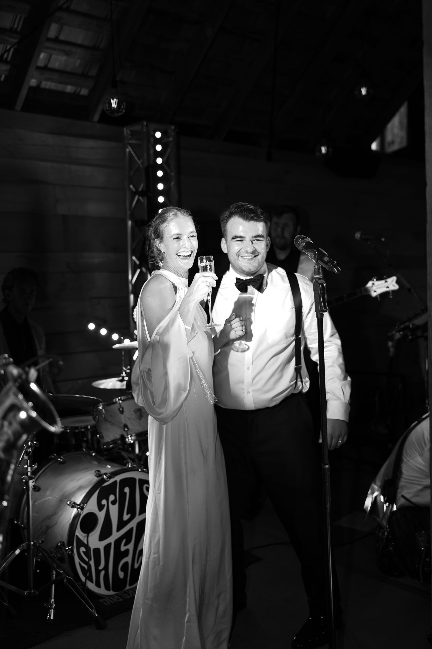 Black and white photo of bride and groom toasting champagne near live band at wedding reception.