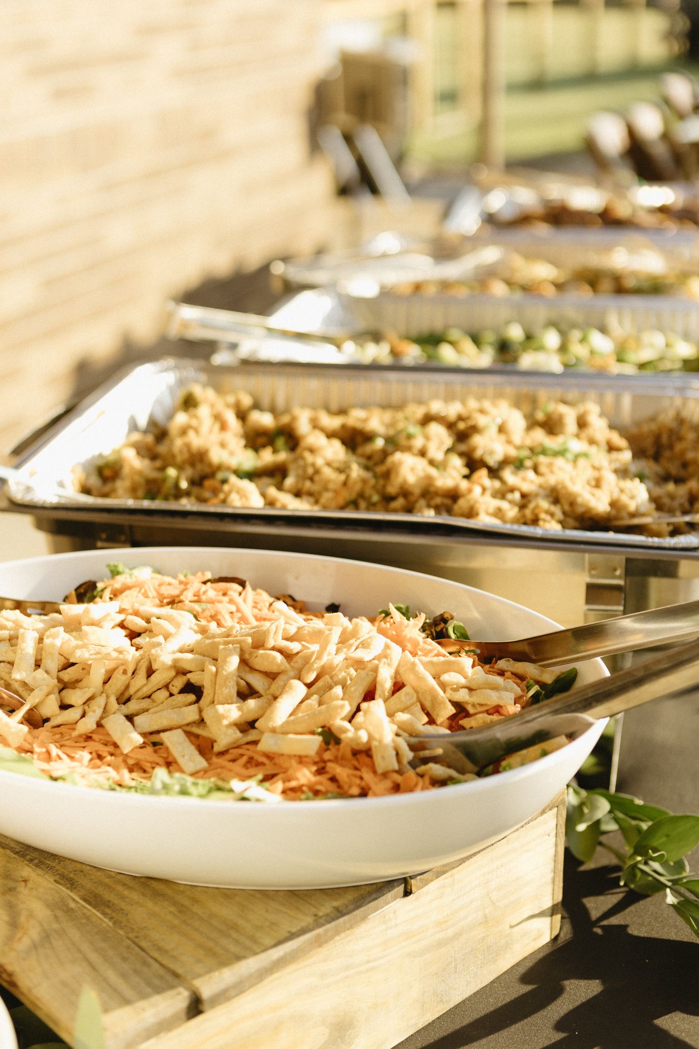 A buffet line featuring various dishes in white serving bowls arranged on wooden platforms.