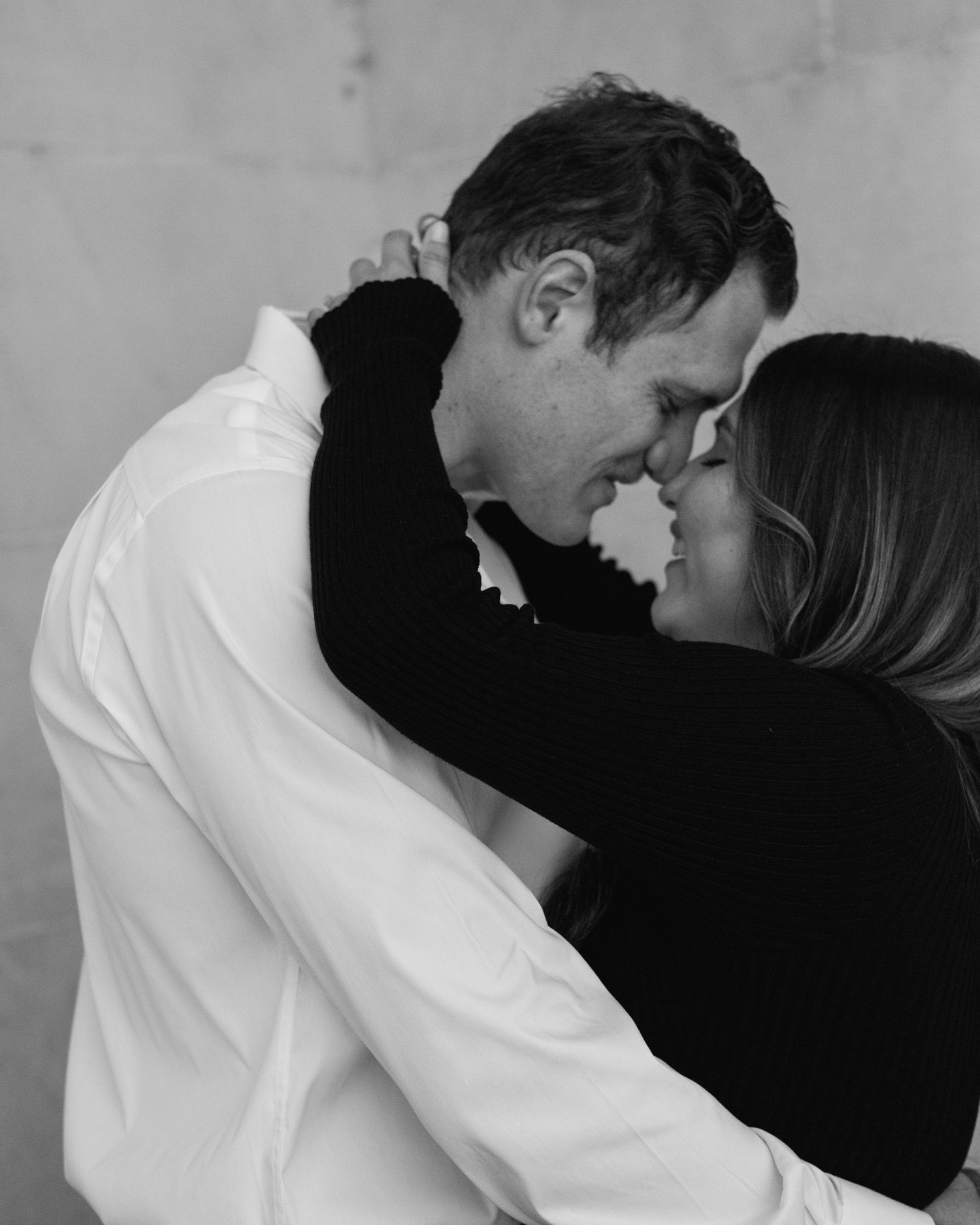 Engaged couple in downtown Louisville, with the woman smiling and showing her engagement ring while embracing her fiancé