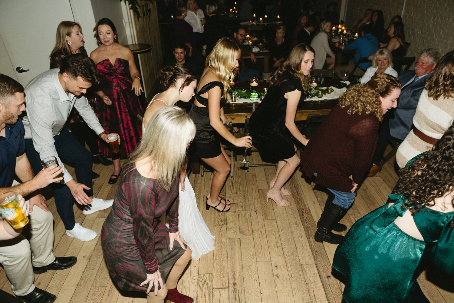 Energetic dancing at a wedding reception on a wooden floor with party lights in the background.