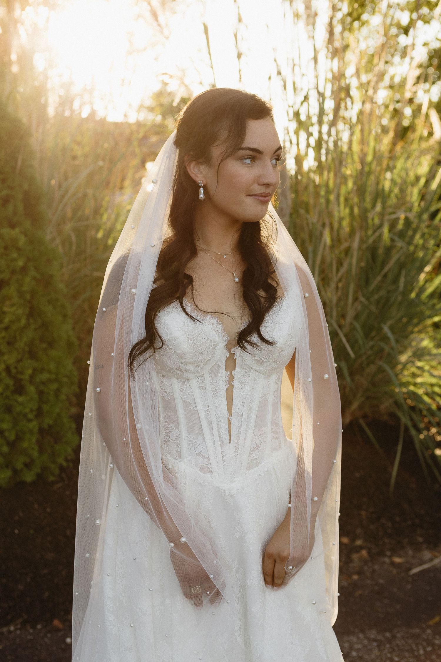 Bride in a white dress with pearl details posing in golden sunset light.
