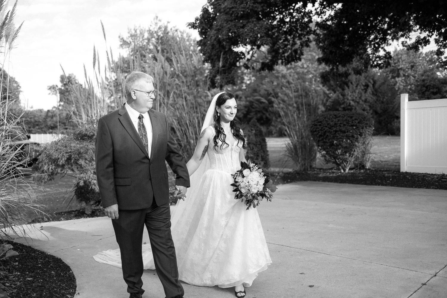 Wedding couple walks together on outdoor pathway surrounded by greenery.