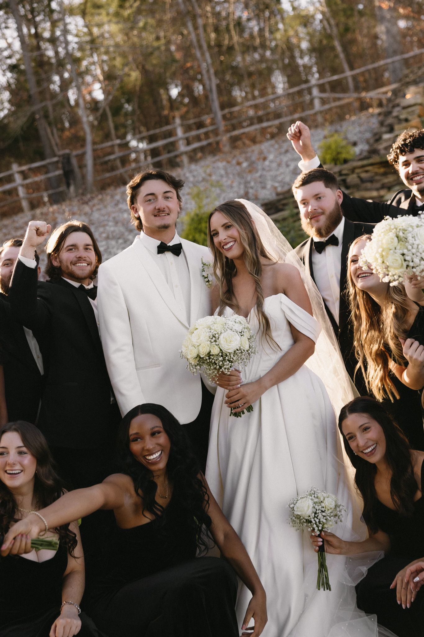 Wedding party in black and white attire posing together outdoors with joyful expressions.