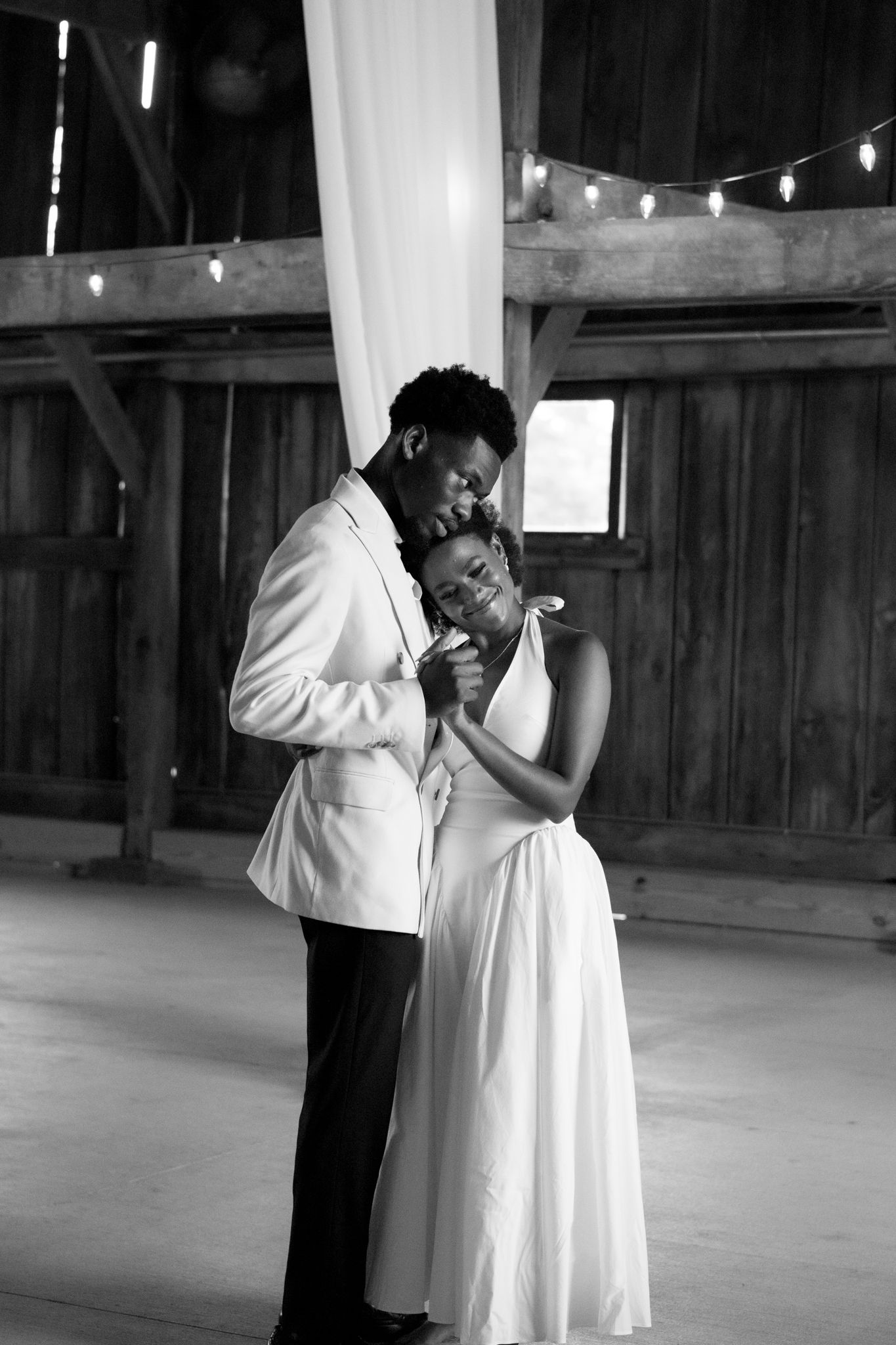Intimate wedding dance captured in rustic barn setting with string lights.