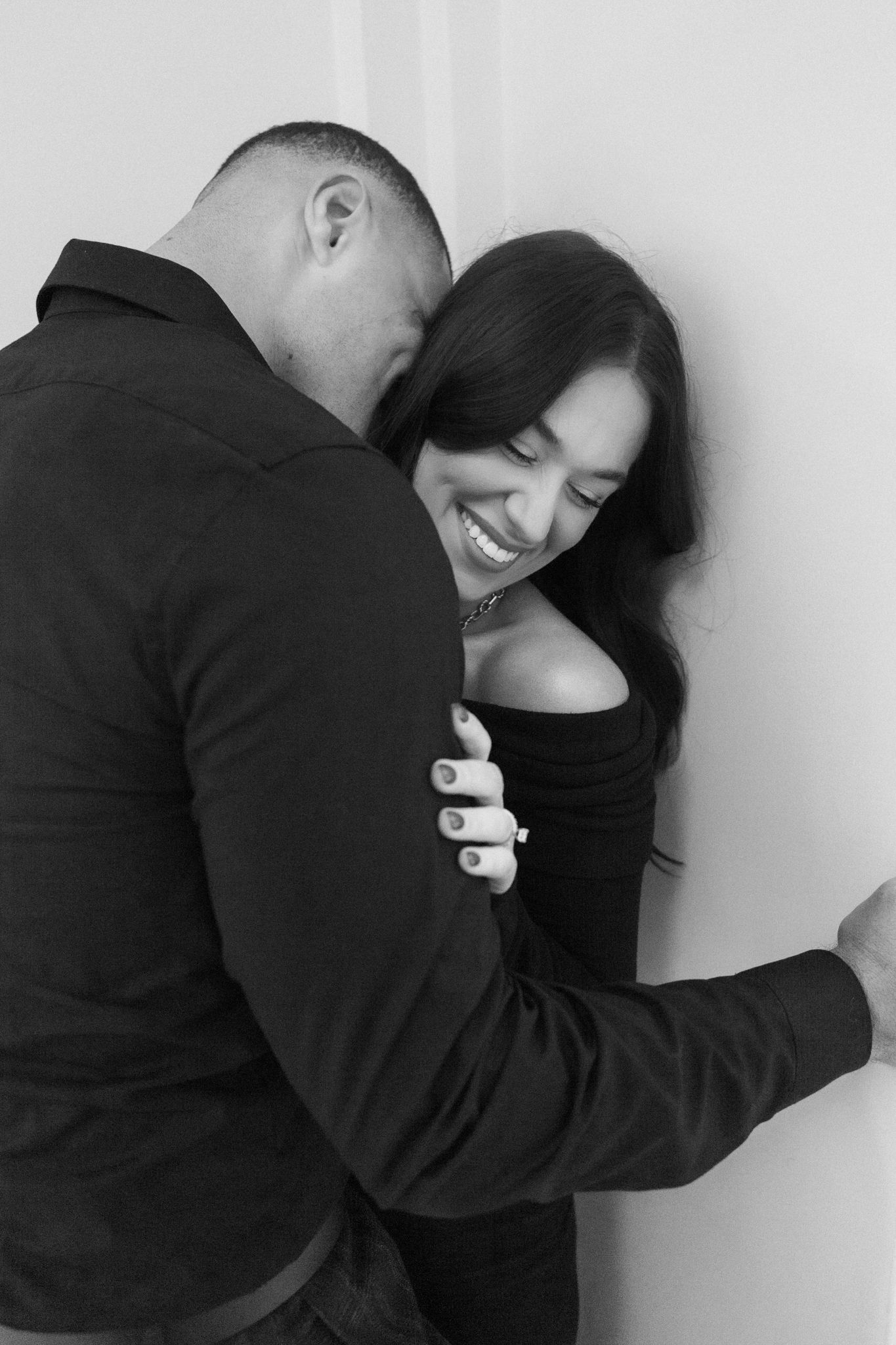 A romantic black and white portrait of a couple sharing an intimate moment against a wall.