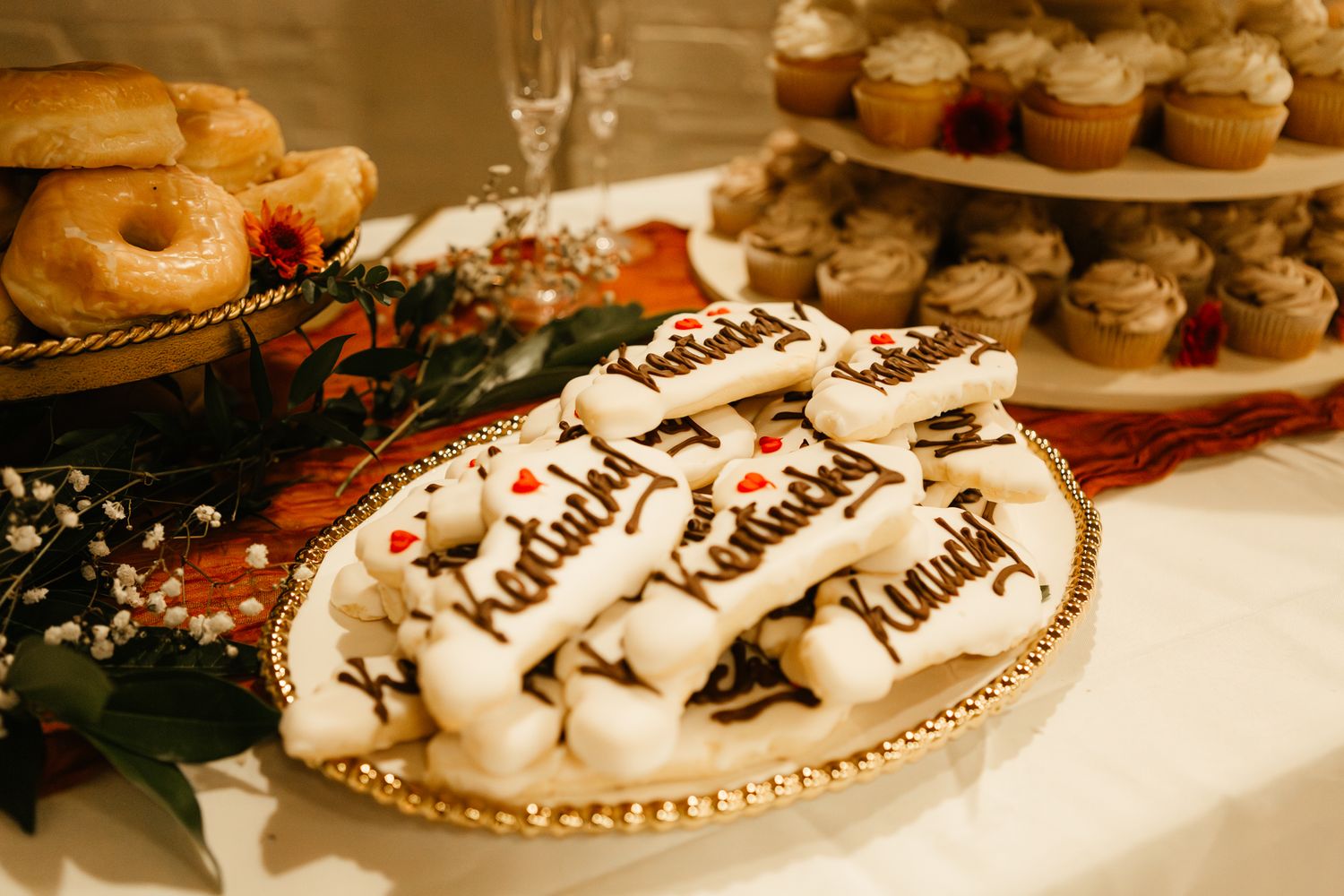 Decorated sugar cookies displayed on a gold-rimmed platter among cupcakes and holiday greenery.