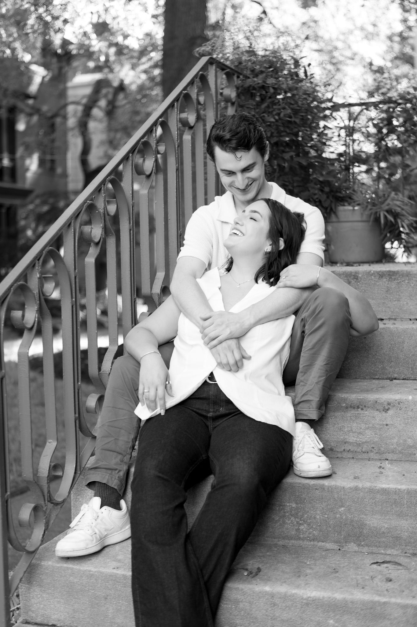 A romantic black and white photo of a couple sharing an intimate moment on outdoor stone steps with an ornate railing.