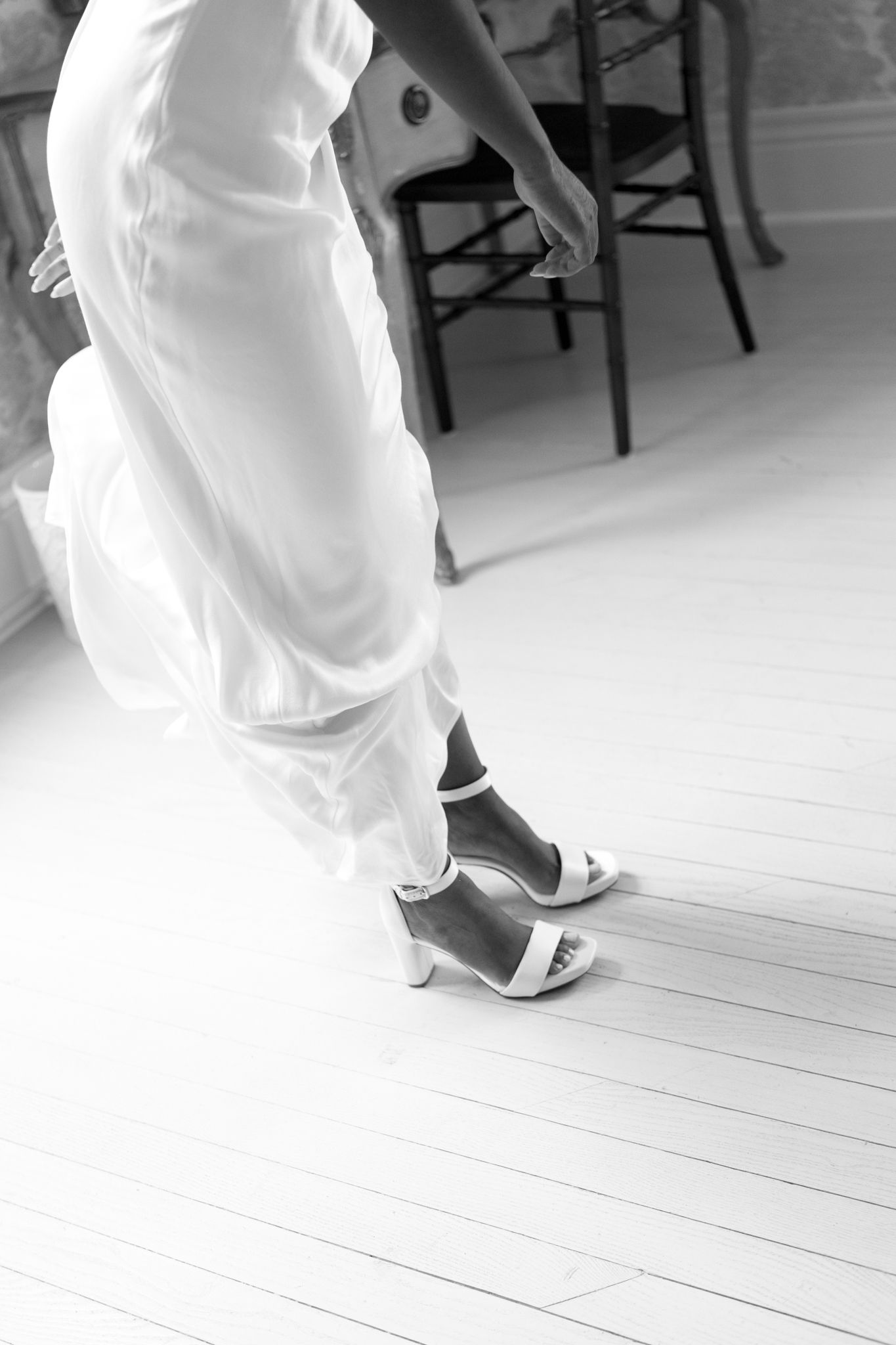 Close-up detail of elegant white wedding shoes on a light wooden floor during a dance.