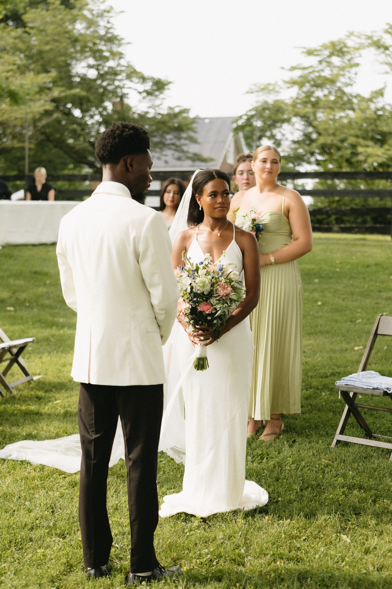 Wedding party members in formal attire walk across a green lawn during an outdoor ceremony.
