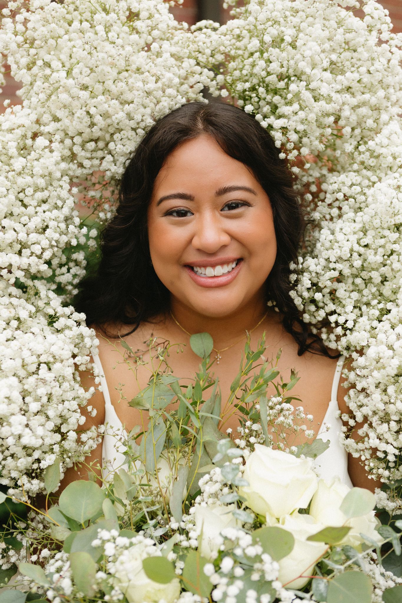 Bride surrounded by delicate baby's breath and eucalyptus holding white floral bouquet in romantic outdoor portrait.