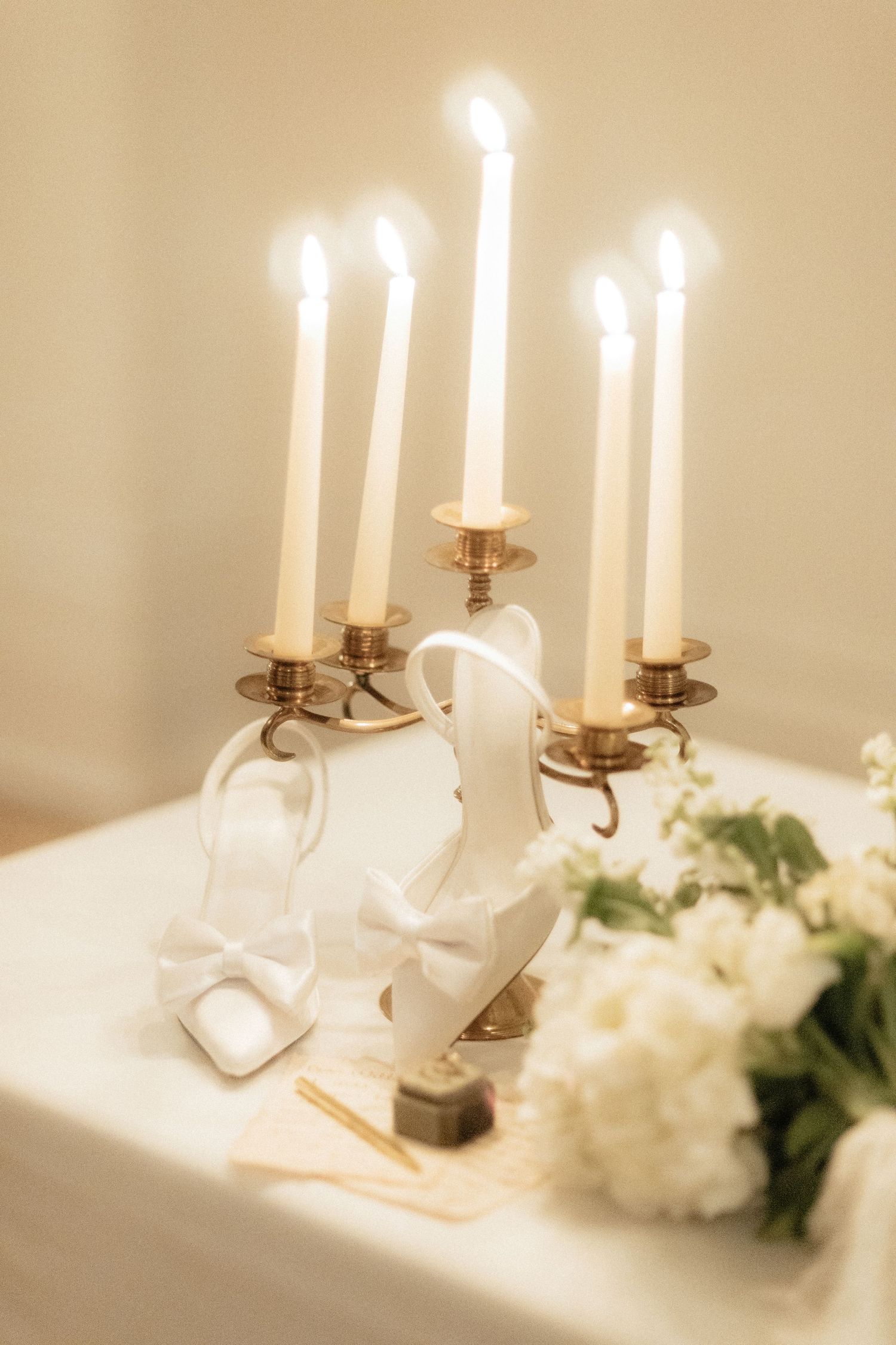 Elegant wedding table with lit gold candelabra, white floral bouquet, and decorative figurines on a white tablecloth.