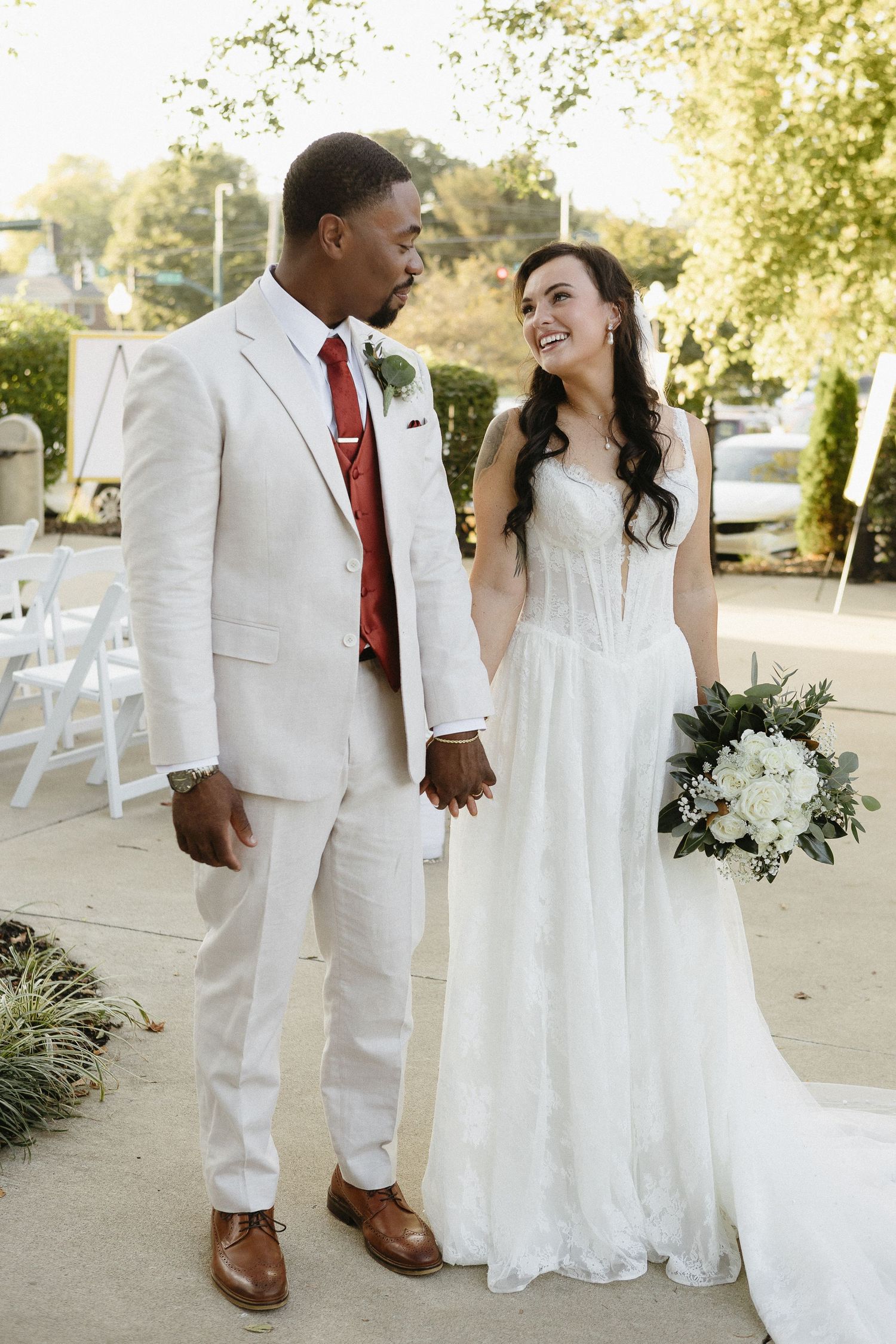 Wedding couple in crisp white attire with burgundy accents posing outdoors.