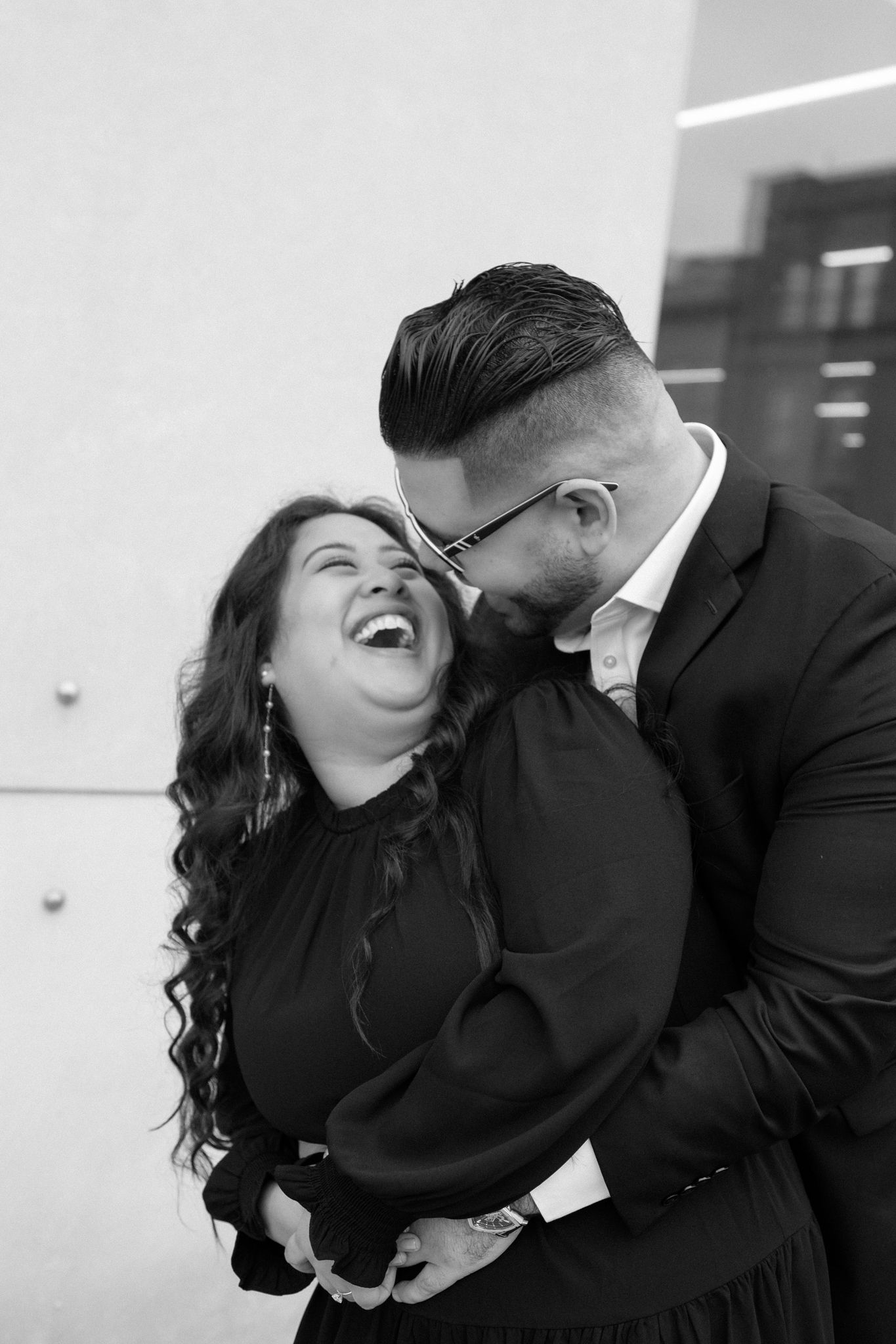 Engaged couple in downtown Louisville, with the woman smiling and showing her engagement ring while embracing her fiancé