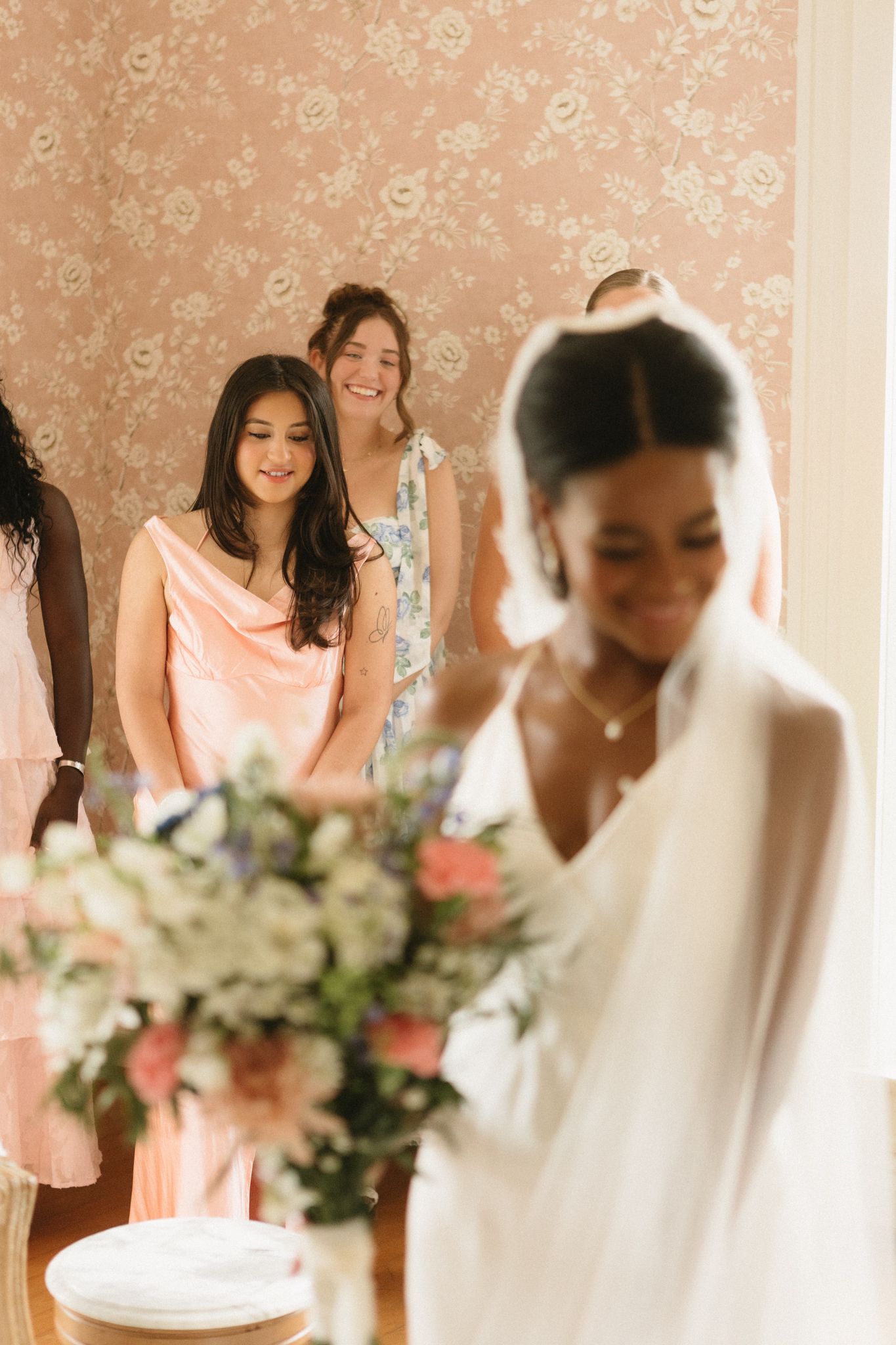 Wedding party in peach and white dresses preparing with floral bouquets.