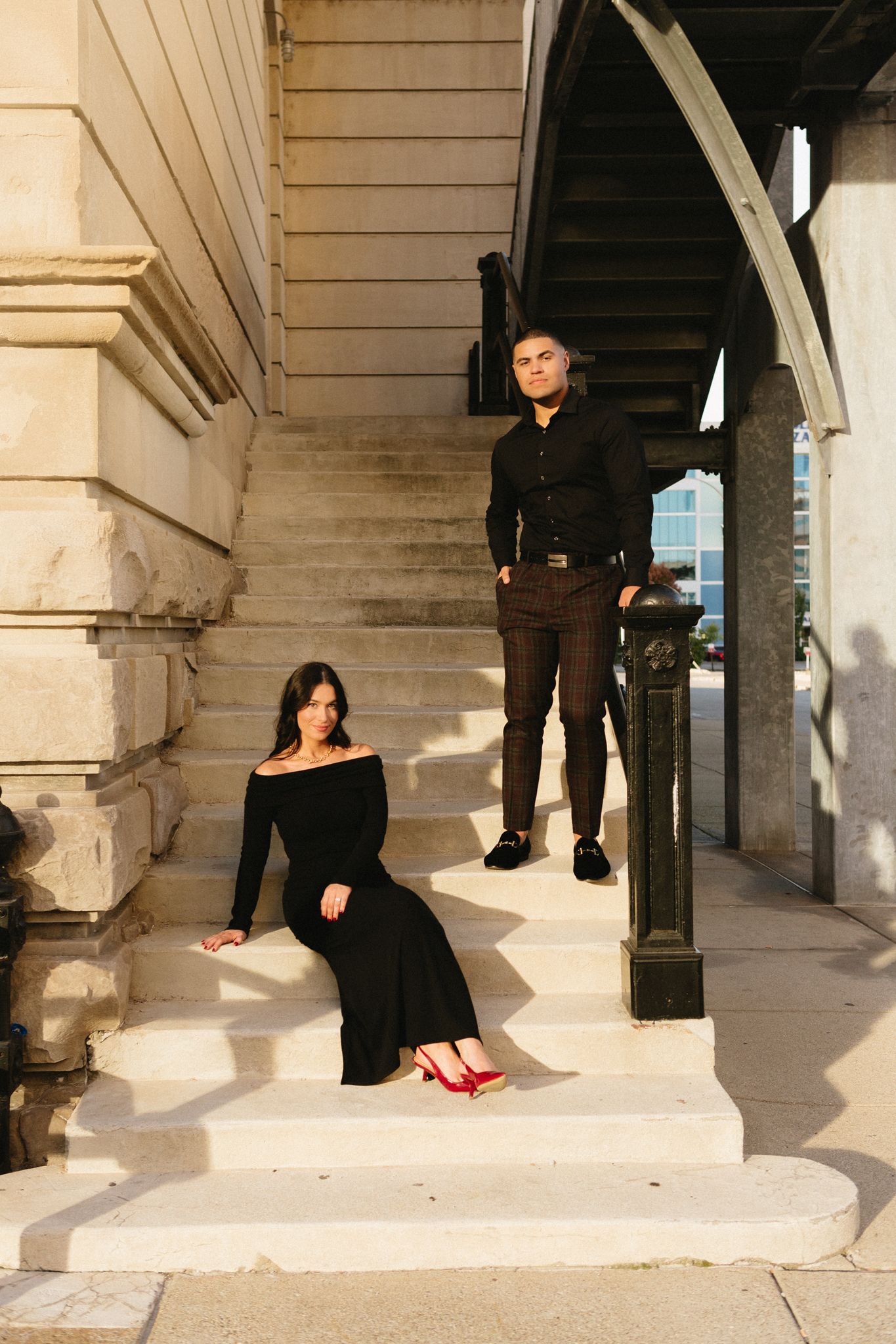 A couple poses dramatically on outdoor stone steps with arched architectural details.