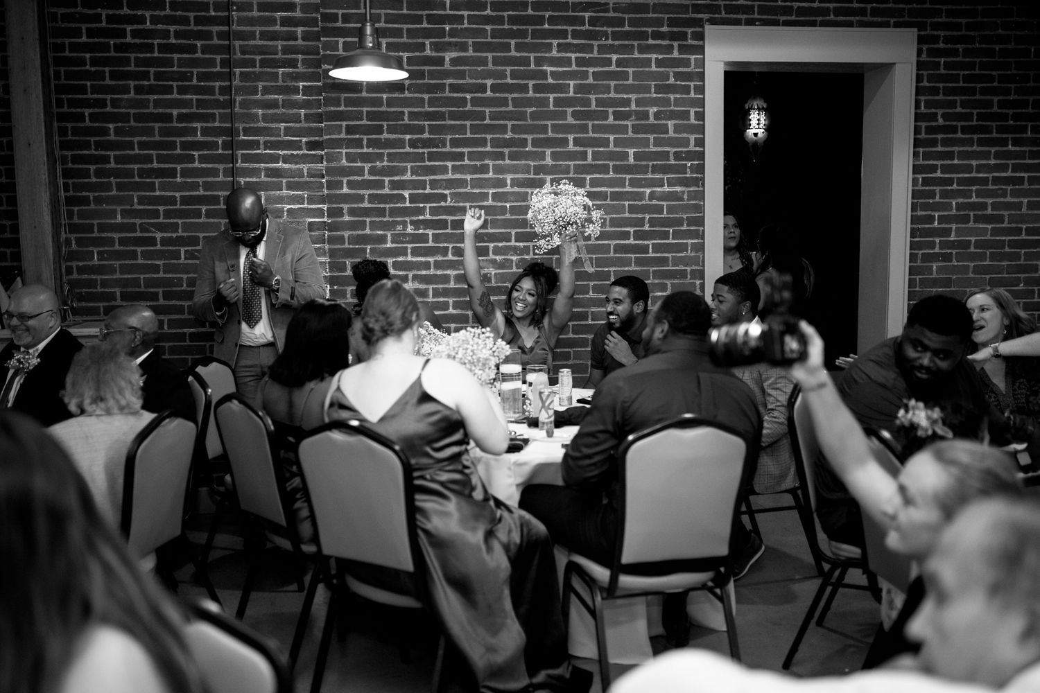 Group of people gathered around tables having a meeting or discussion in a brick-walled room.