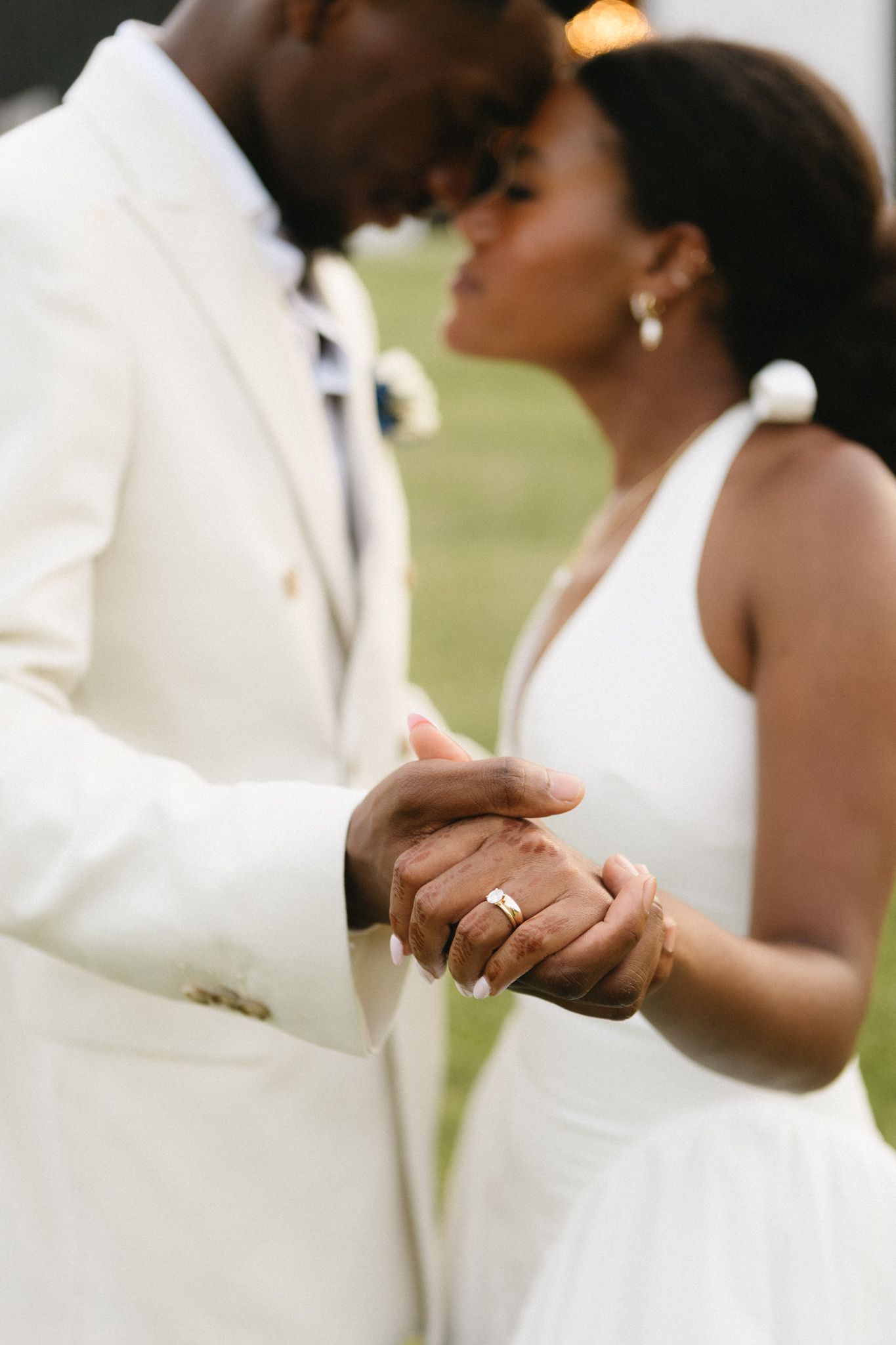 Close-up details of a couple holding hands showing wedding rings against white formal attire.